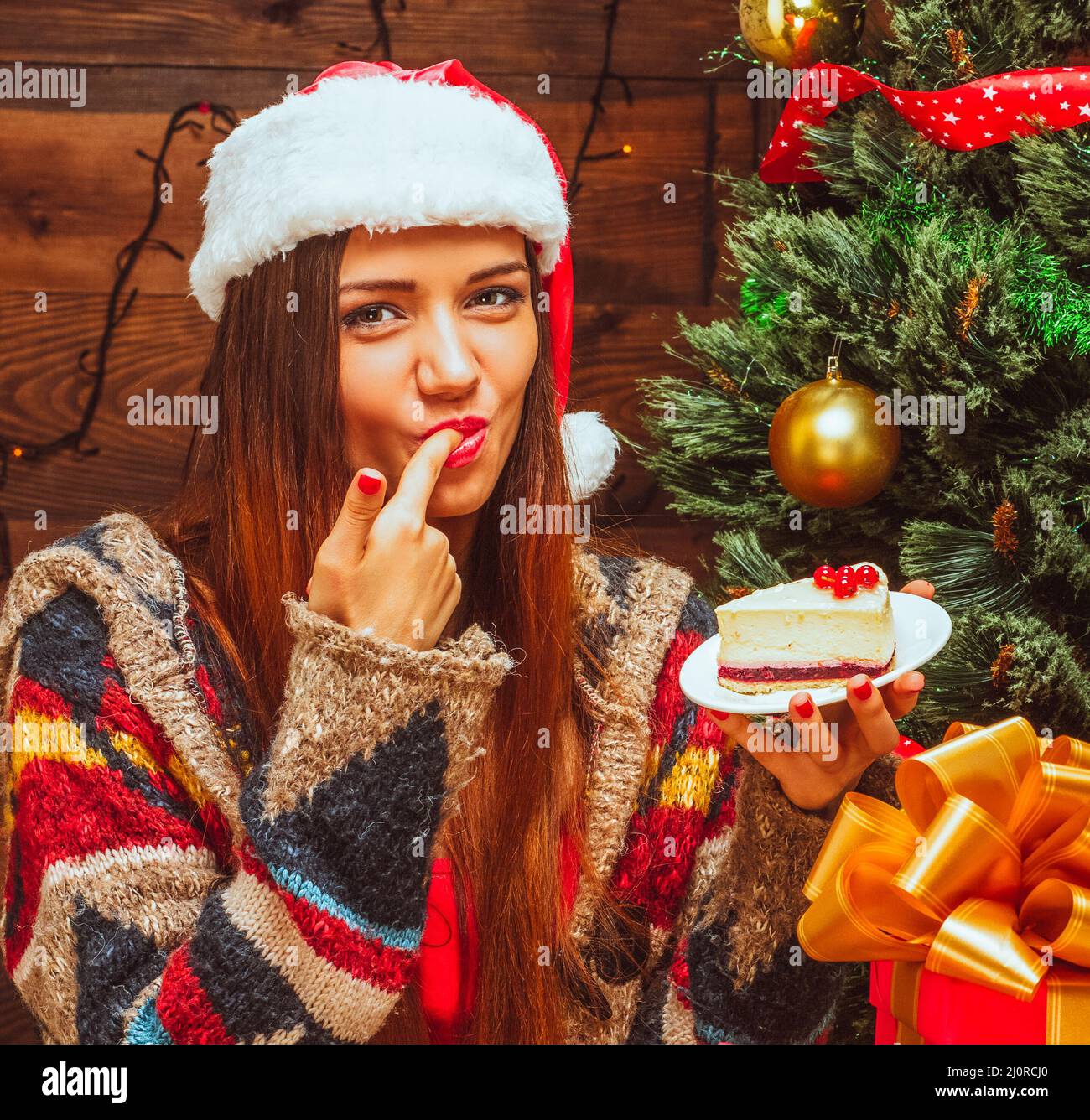 Bright lady holding a plate with a slice of cake and tasting it, finger in the mouth, Christmas Eve, Christmas dinner, Christmas Stock Photo