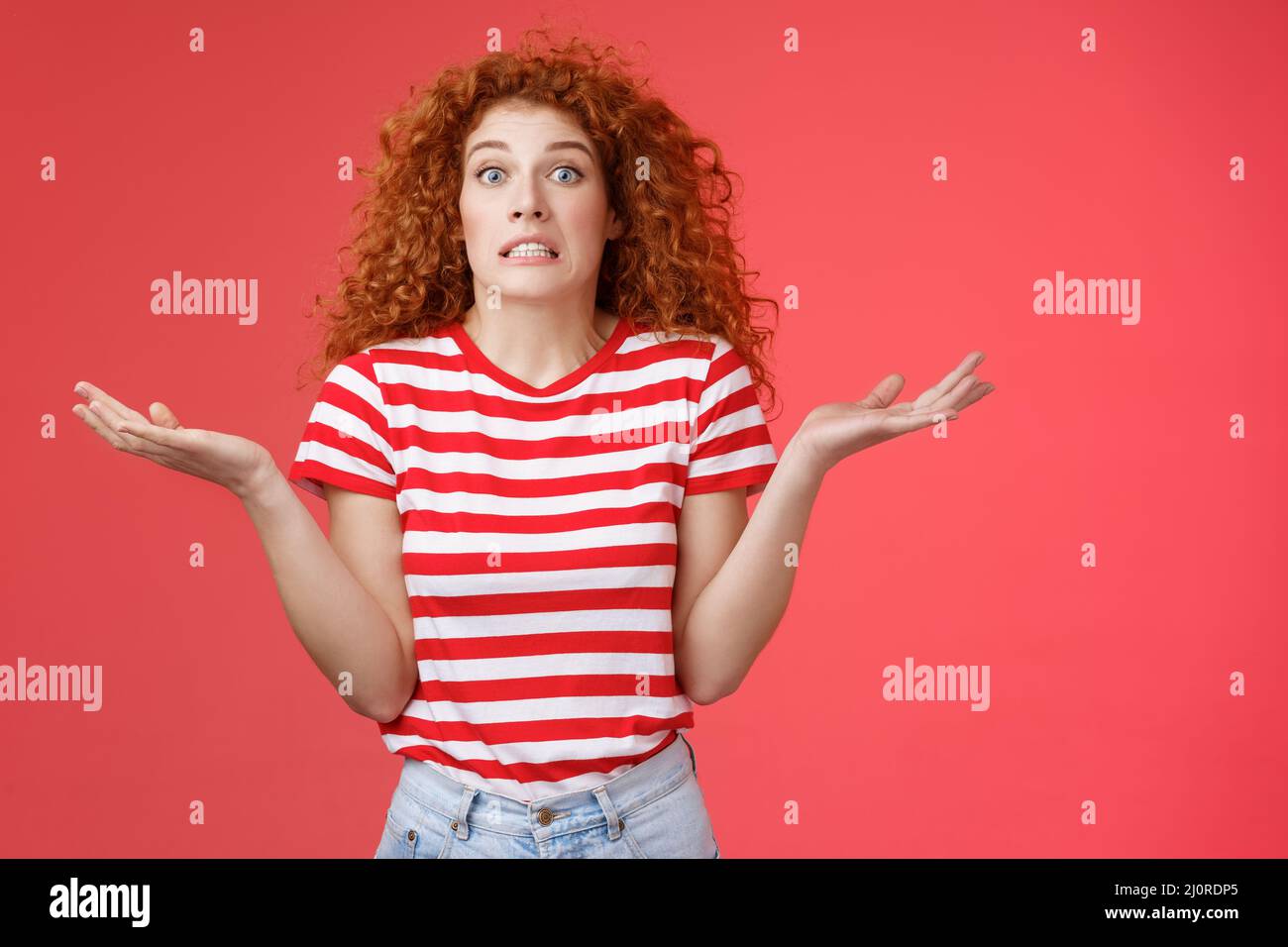 Yikes how should I know. Unaware worried awkward cute redhead curly girl clench teeth smirking uncertain panic cannot answer pop Stock Photo
