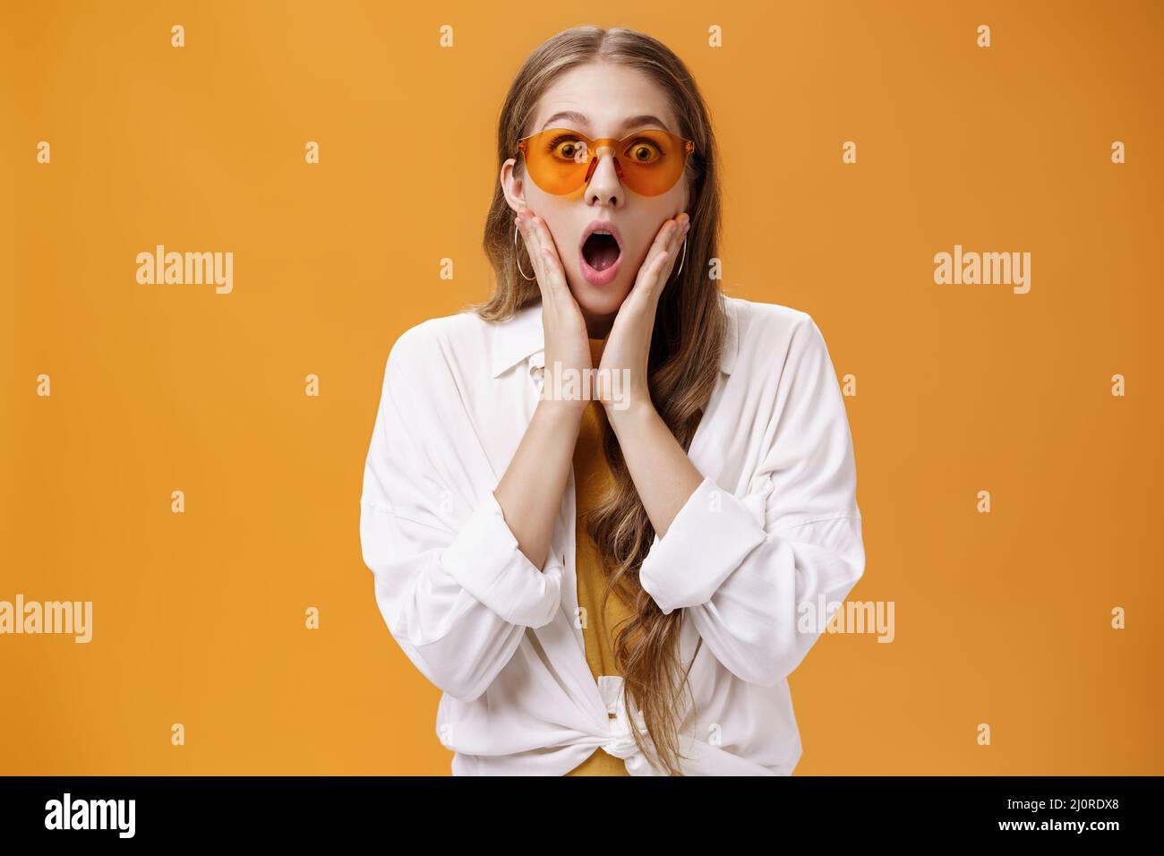 Waist-up shot of amazed and surprised party girl in trendy sunglasses and cool outfit gasping from shock standing with opened mo Stock Photo