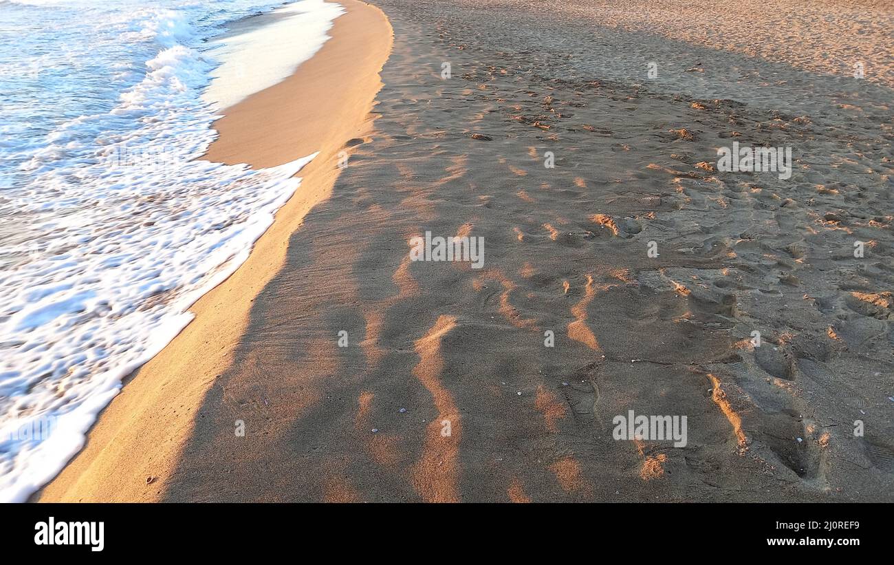 Closeup shot of the waves on the sandy shore at sunset in spring Stock Photo