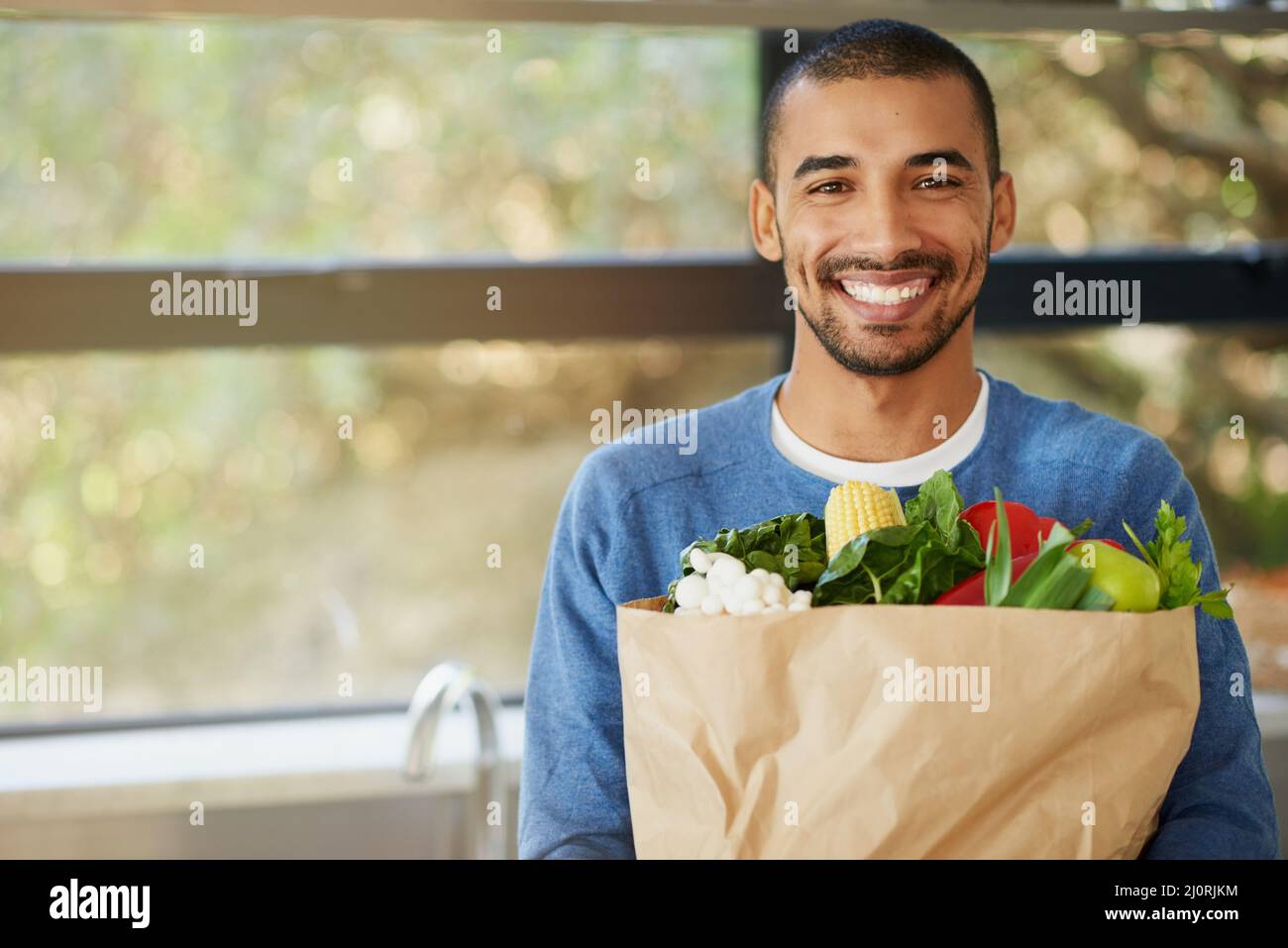 Healthy food motivates me to be my best. Portrait of a happy young man holding a bag full of healthy vegetables at homee. Stock Photo