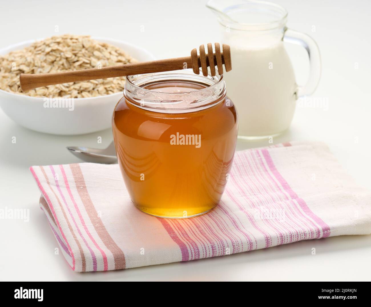honey in a glass transparent jar and a wooden stick on a white table