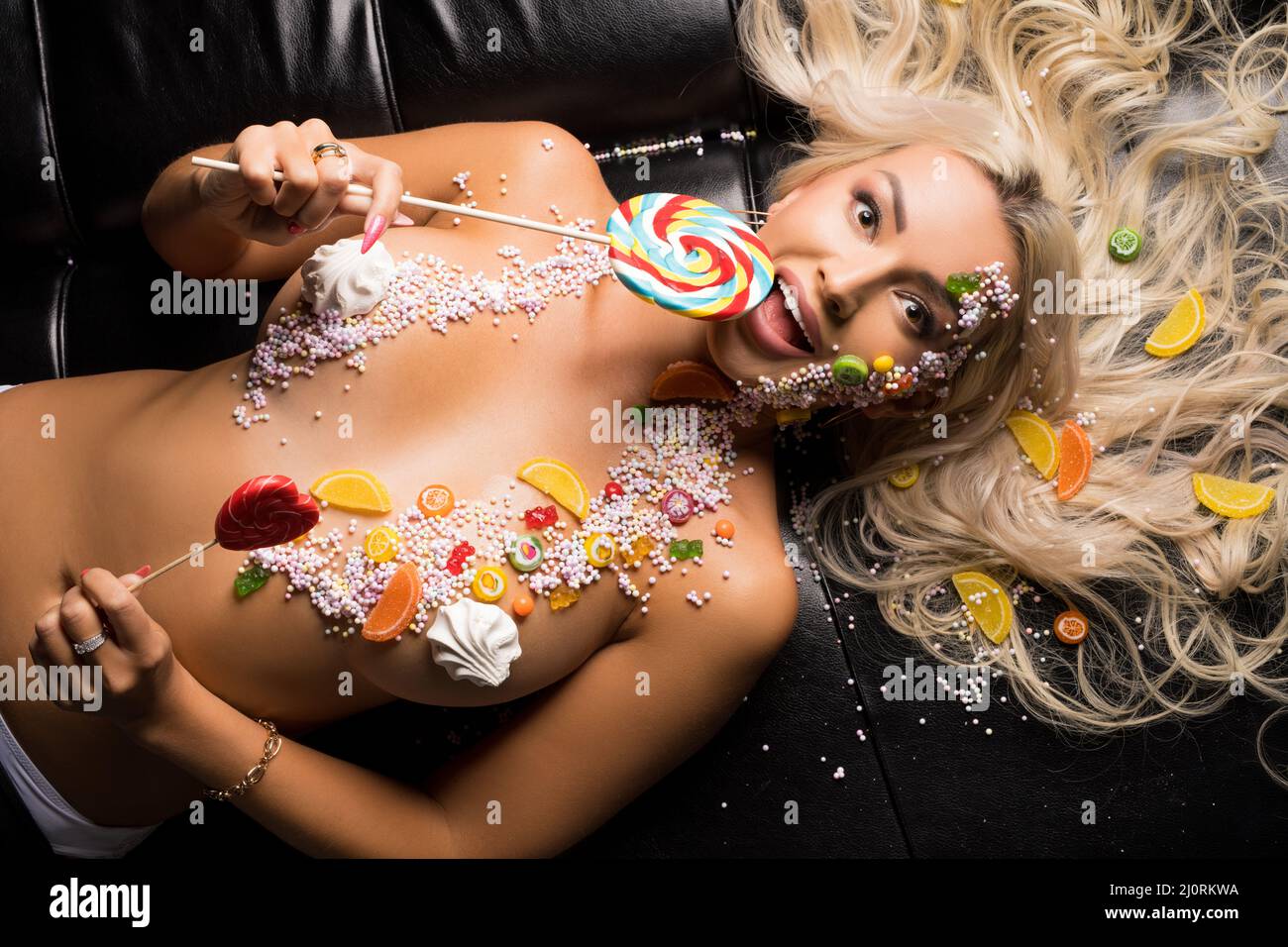 Nude woman licking lollipop on black sofa Stock Photo