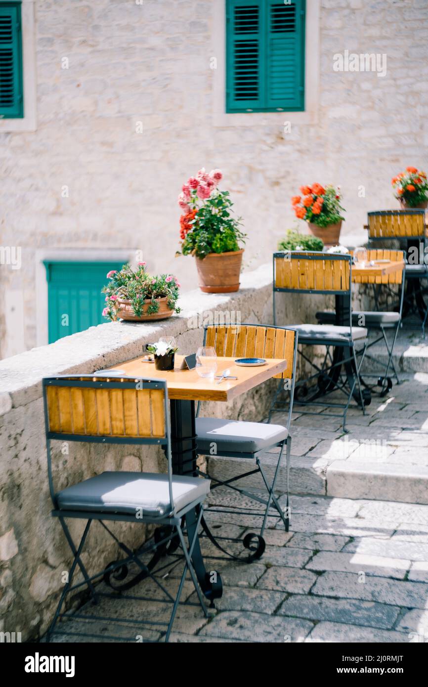 Metal chairs with cushions around square tables on paving stones near a stone building Stock Photo
