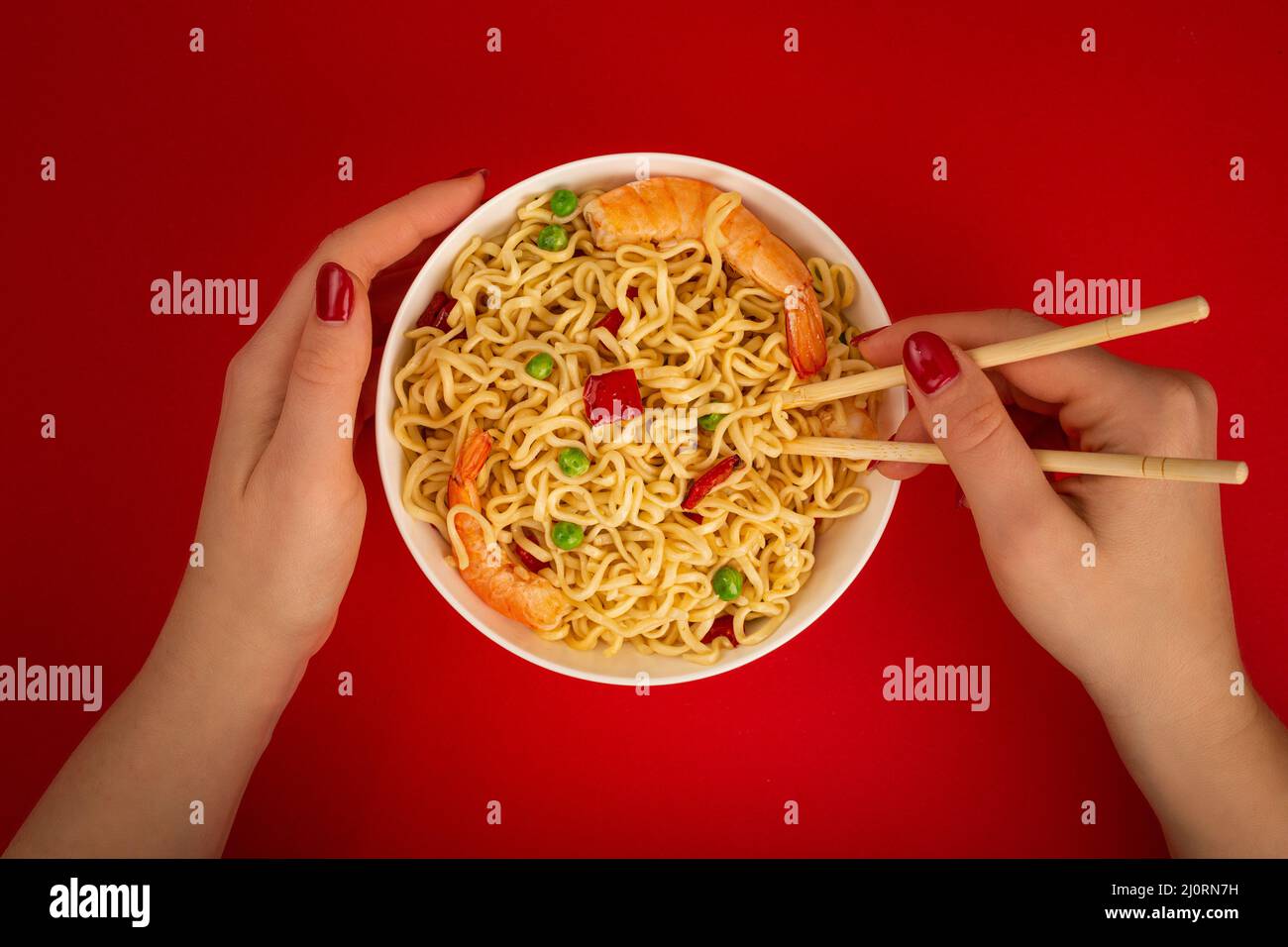 Female hands with bowl of shrimp noodles on red background Stock Photo