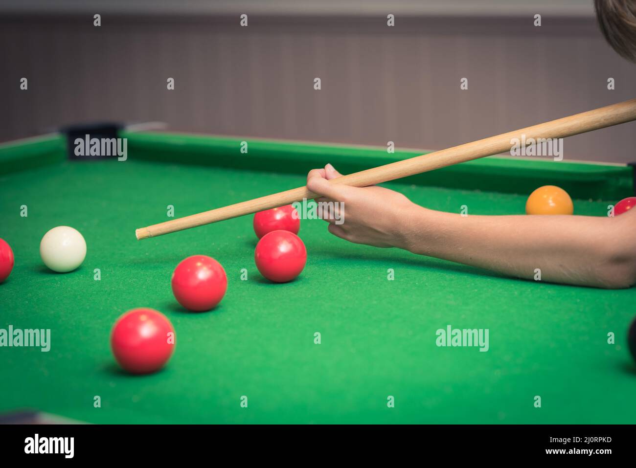 Cute boy in blue t shirt plays billiard or pool in club. Boy with billiard cue strikes the ball on table. Active Leisure, sport, hobby concept Stock Photo