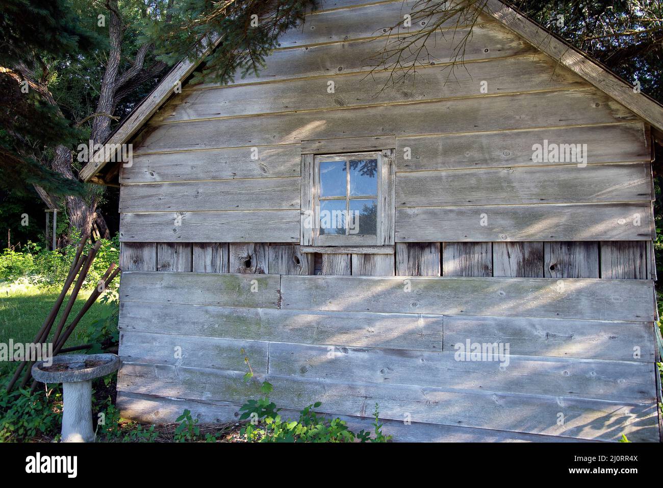 Rustic cabin with stone birdbath and square window in woods Stock Photo