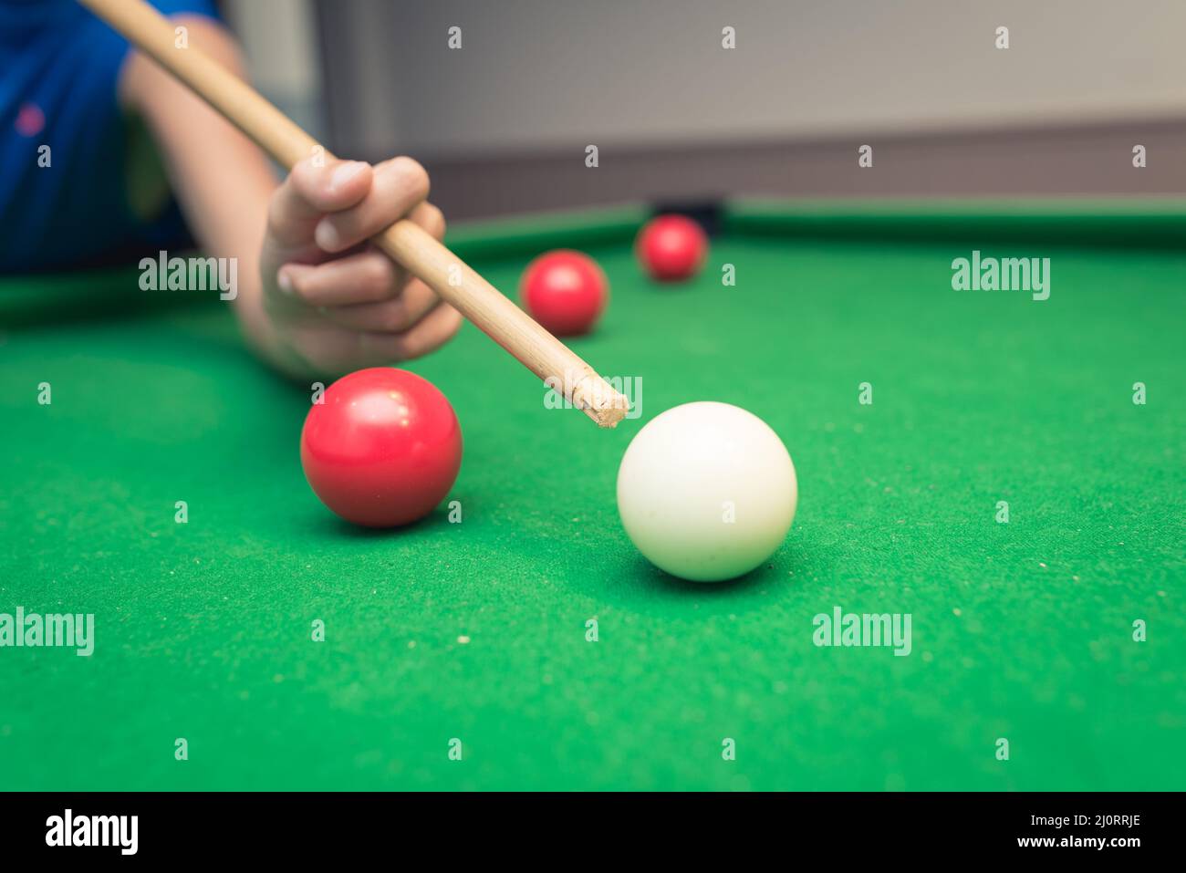 Cute boy in blue t shirt plays billiard or pool in club. Boy with billiard cue strikes the ball on table. Active Leisure, sport, hobby concept Stock Photo