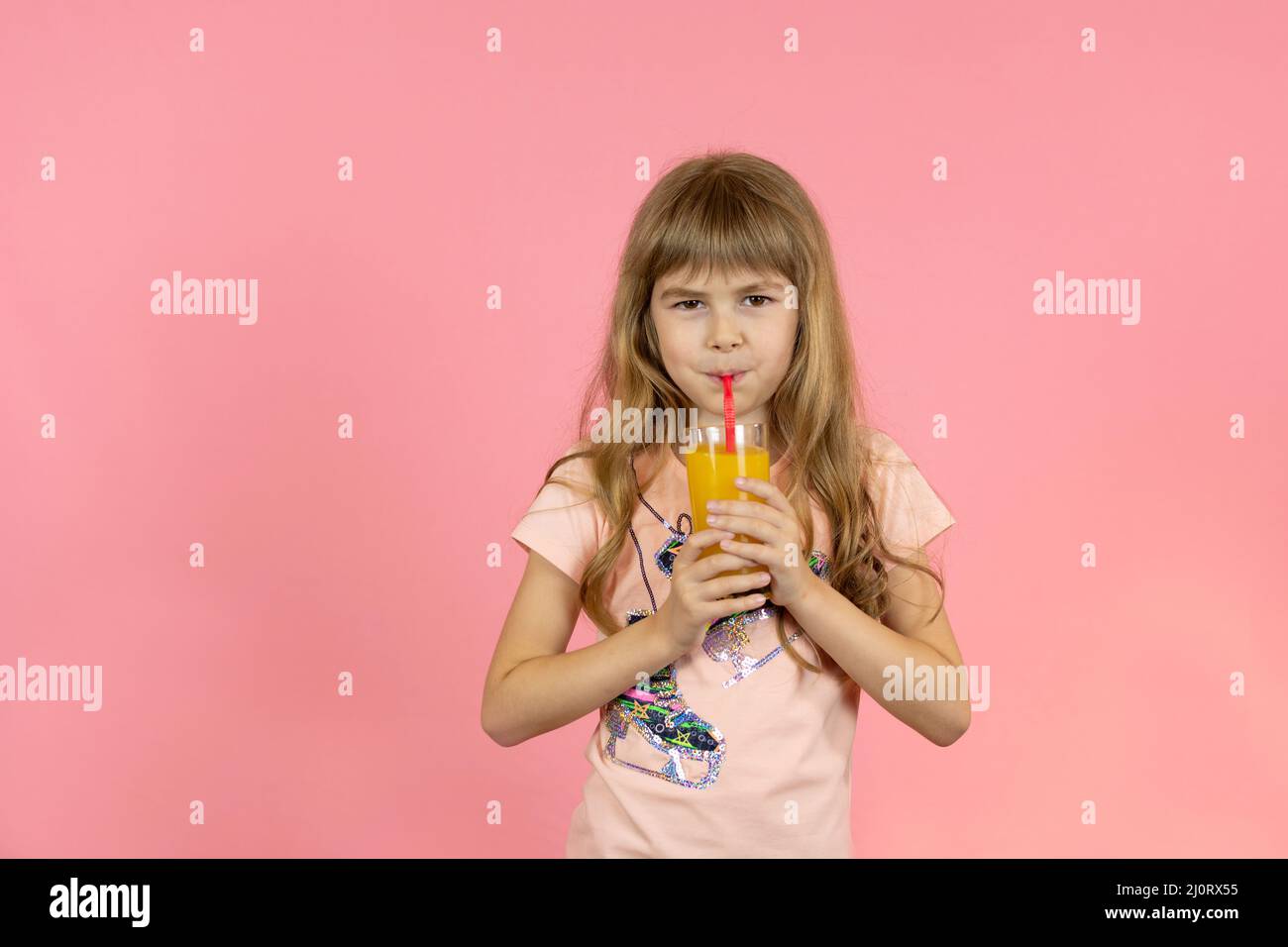 little girl drinks orange juice on a pink background Stock Photo - Alamy