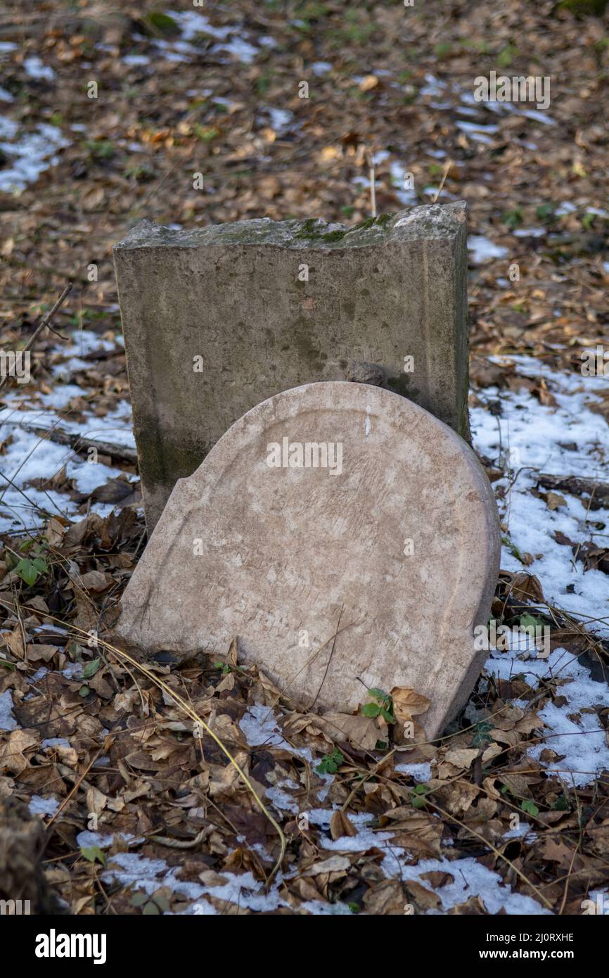Old ancient abandoned jewish cemetery in the forest in the winter. Aged tombstones or gravestones in the graveyard. Stock Photo