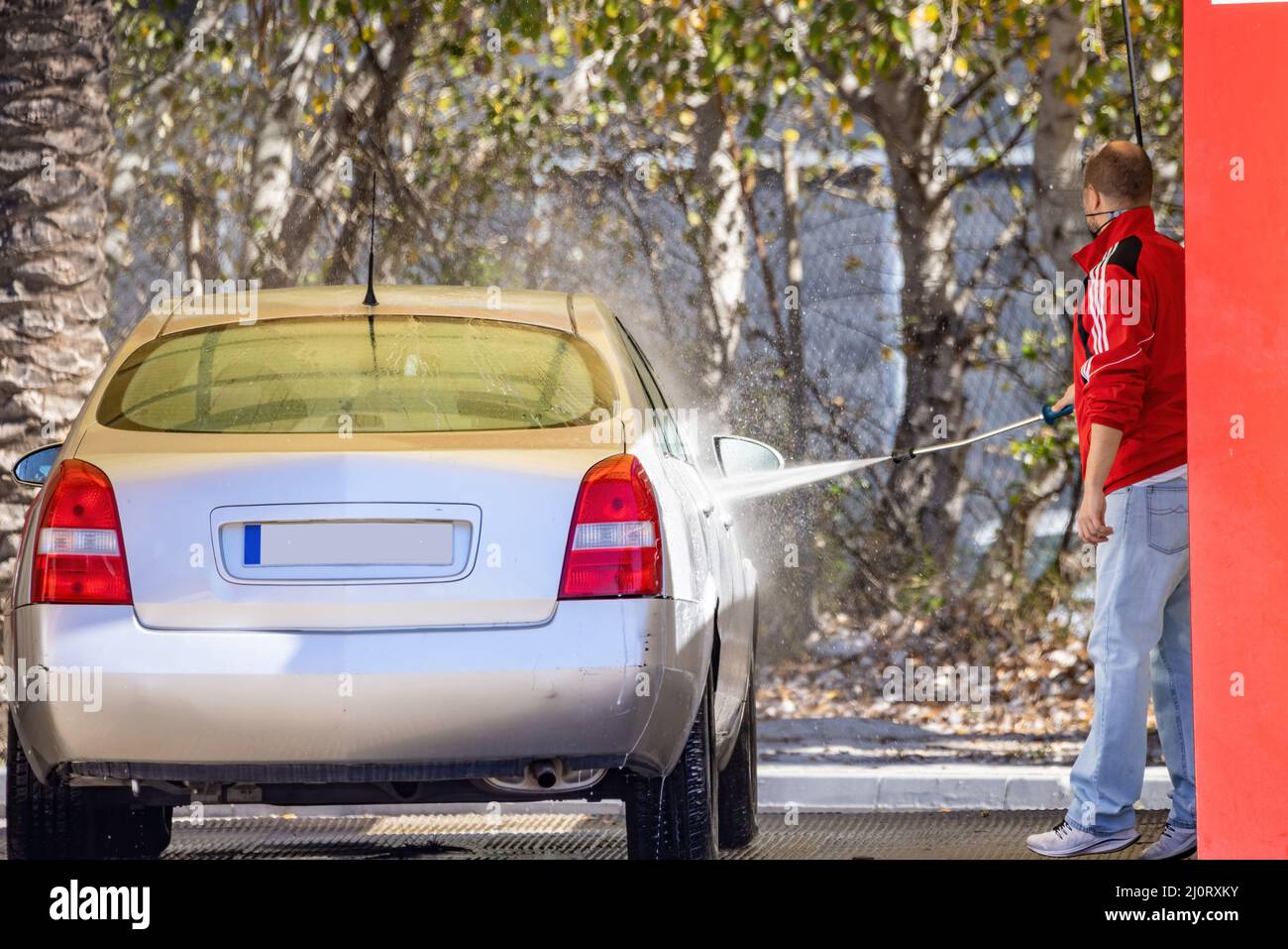An unidentified man is cleaning his car using a high pressure water at service station Stock Photo
