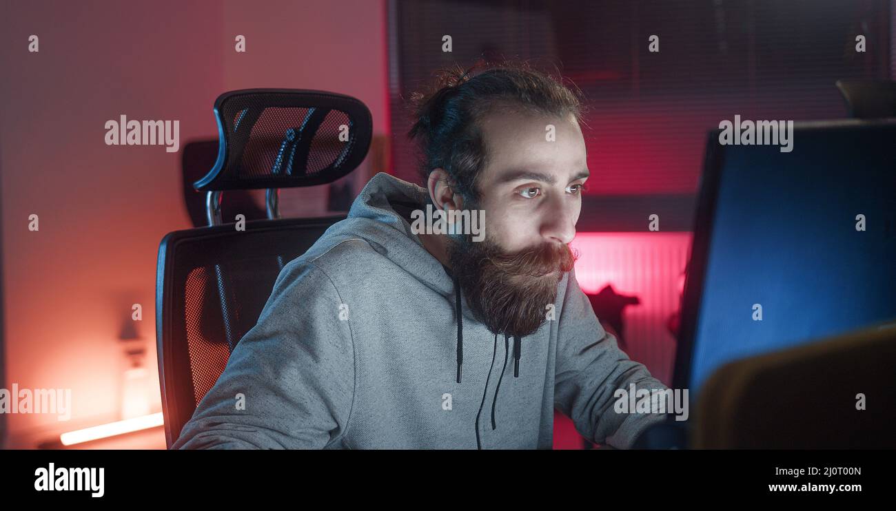 Bearded long-haired hippie looking young adult man playing games at the computer. Stock Photo