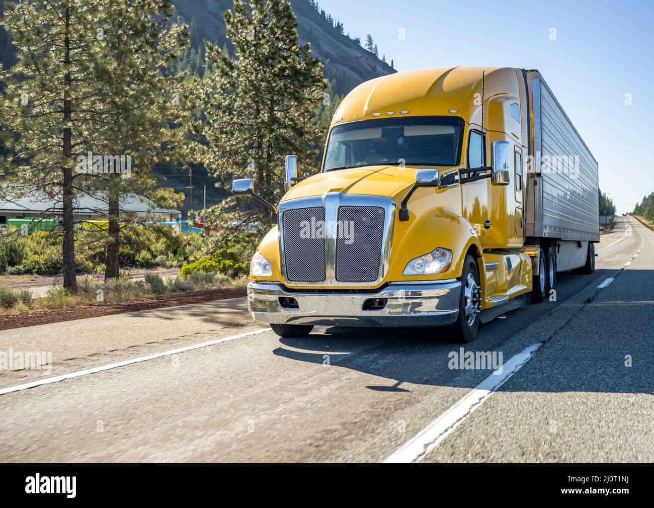 Classic long haul big rig yellow semi truck tractor with truck driver