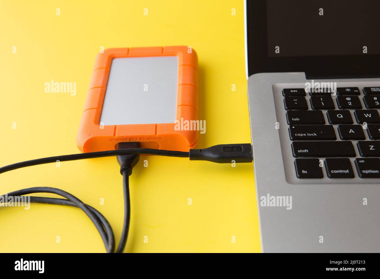 external hard drive on a yellow background connected to a laptop computer USB port Stock Photo