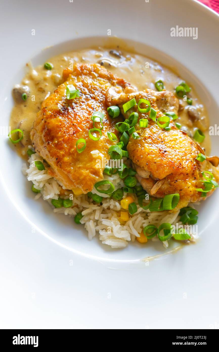 Sautéed boned chicken thighs on a bed of rice with peas and corn served with a rich mushroom , white wine and cream sauce. Homemade family cooking Stock Photo