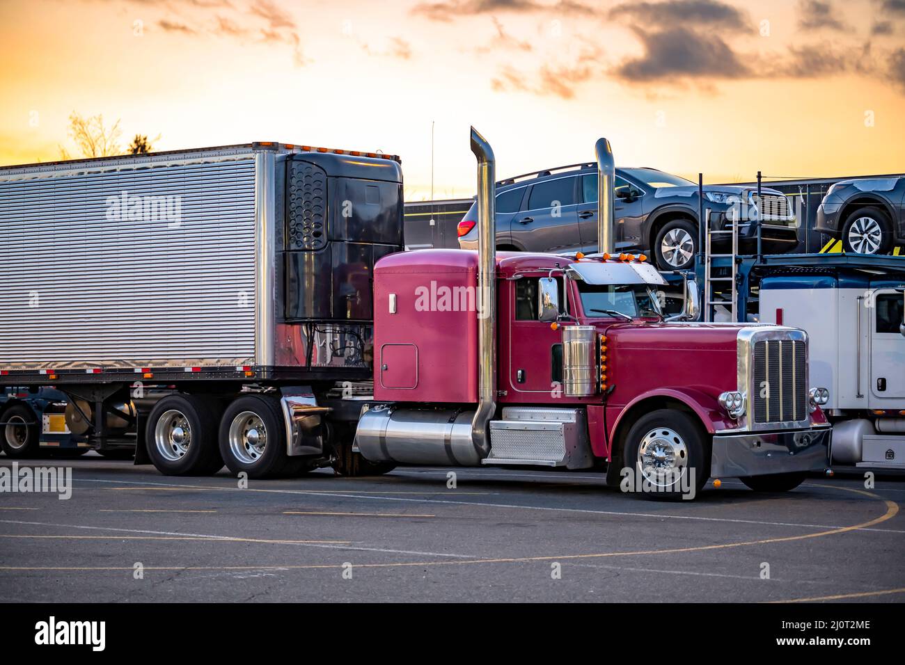 Different models of big rigs semi trucks tractors with car hauler and refrigerator and dry van semi trailers standing in row on the truck stop industr Stock Photo