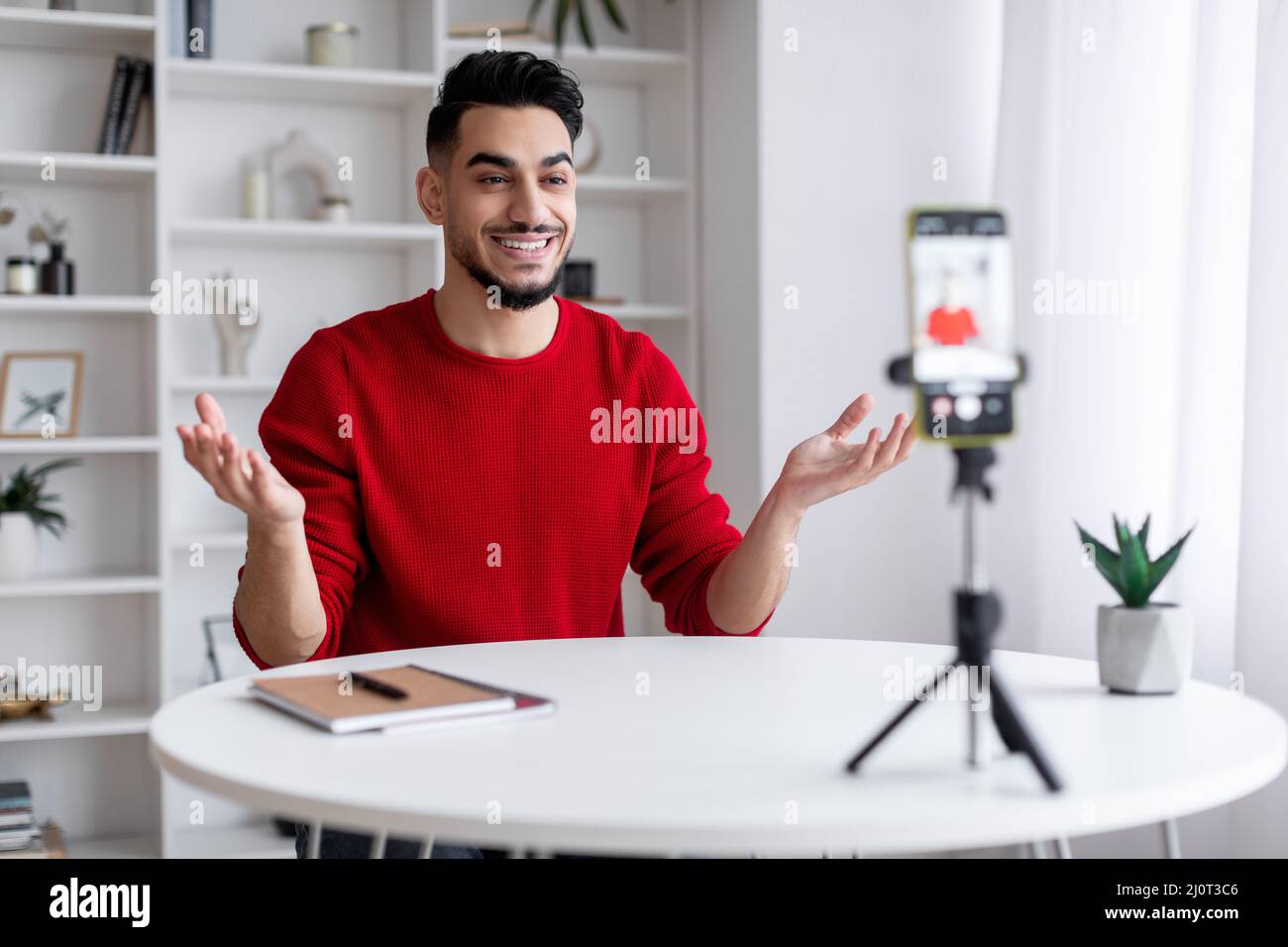 Young Arab Male Blogger Recording Video At Home With Smartphone On Tripod Stock Photo