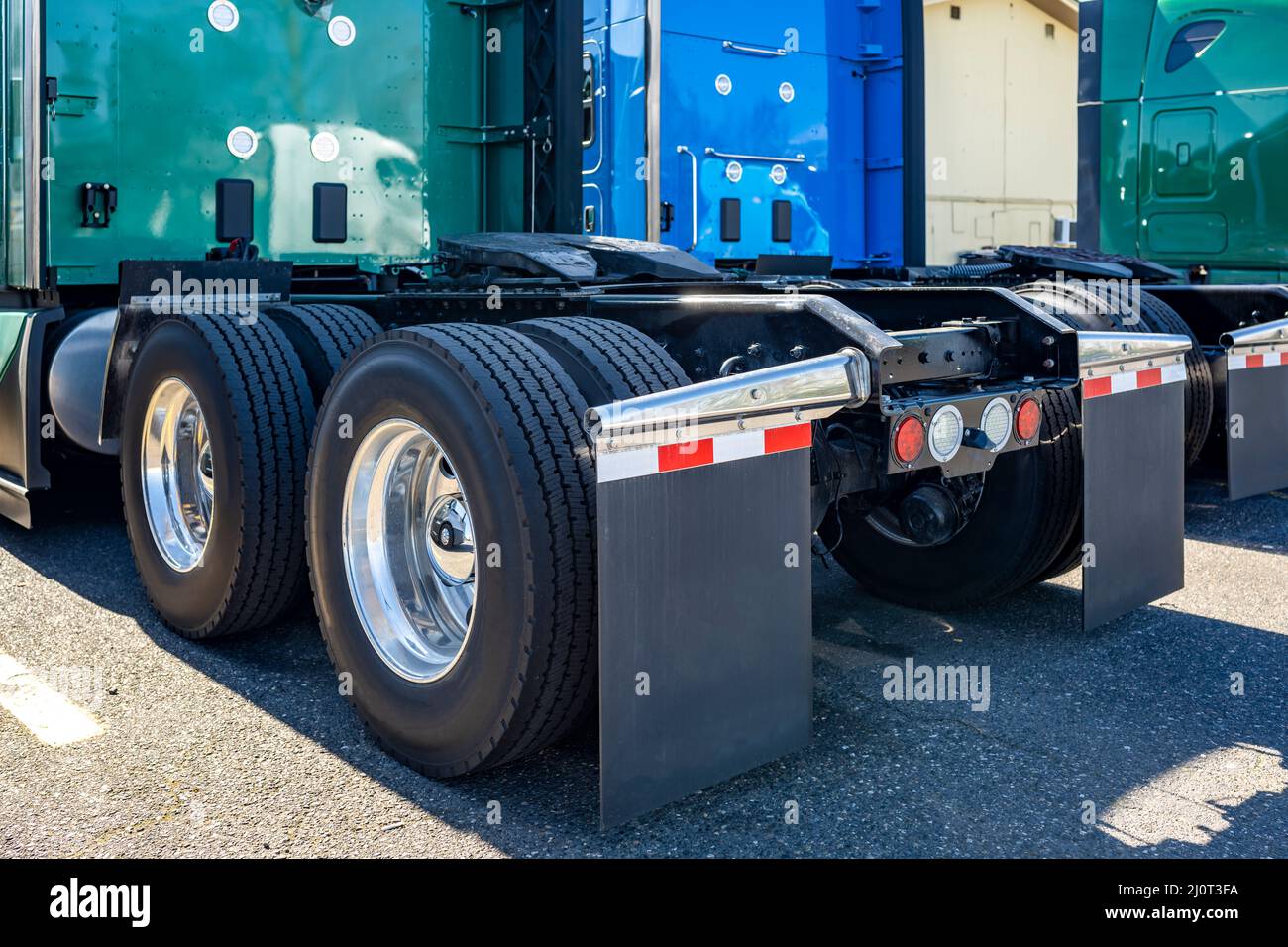 Industrial grade powerful big rigs semi trucks tractors with double wheels on the axles with large tread pattern on tires for better grip standing on Stock Photo