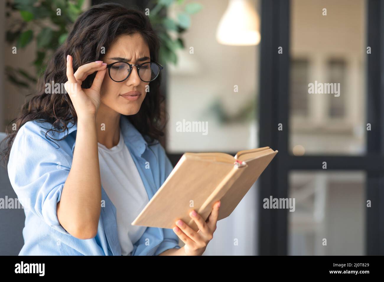Young woman in glasses reading book, having poor eyesight at