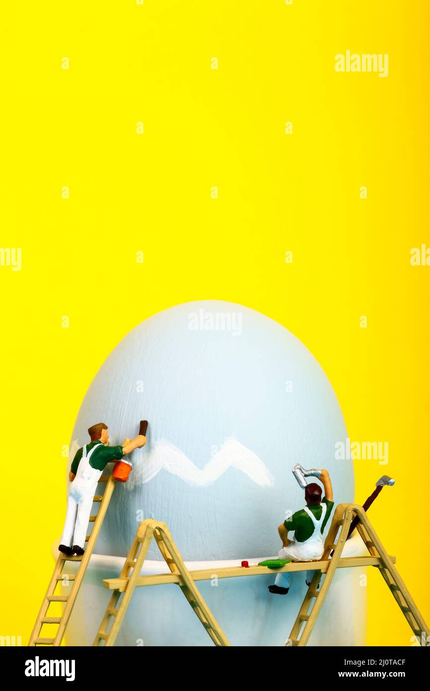 Conceptual image of miniature figure people painting a hens egg for Easter with copy space Stock Photo