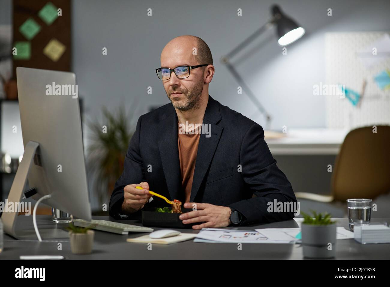 Portrait Of Mature Businessman Eating Takeout Dinner At Workplace While Portrait Of Mature Businessman Eating Takeout Dinner At Workplace While