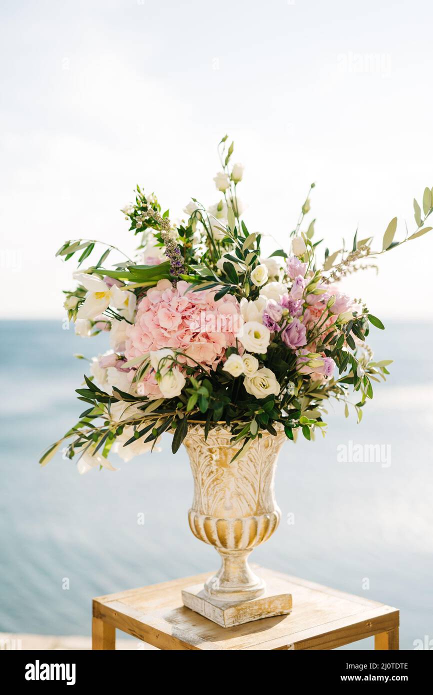 Bouquet of flowers in an antique vase stands on a stool against the background of water Stock Photo