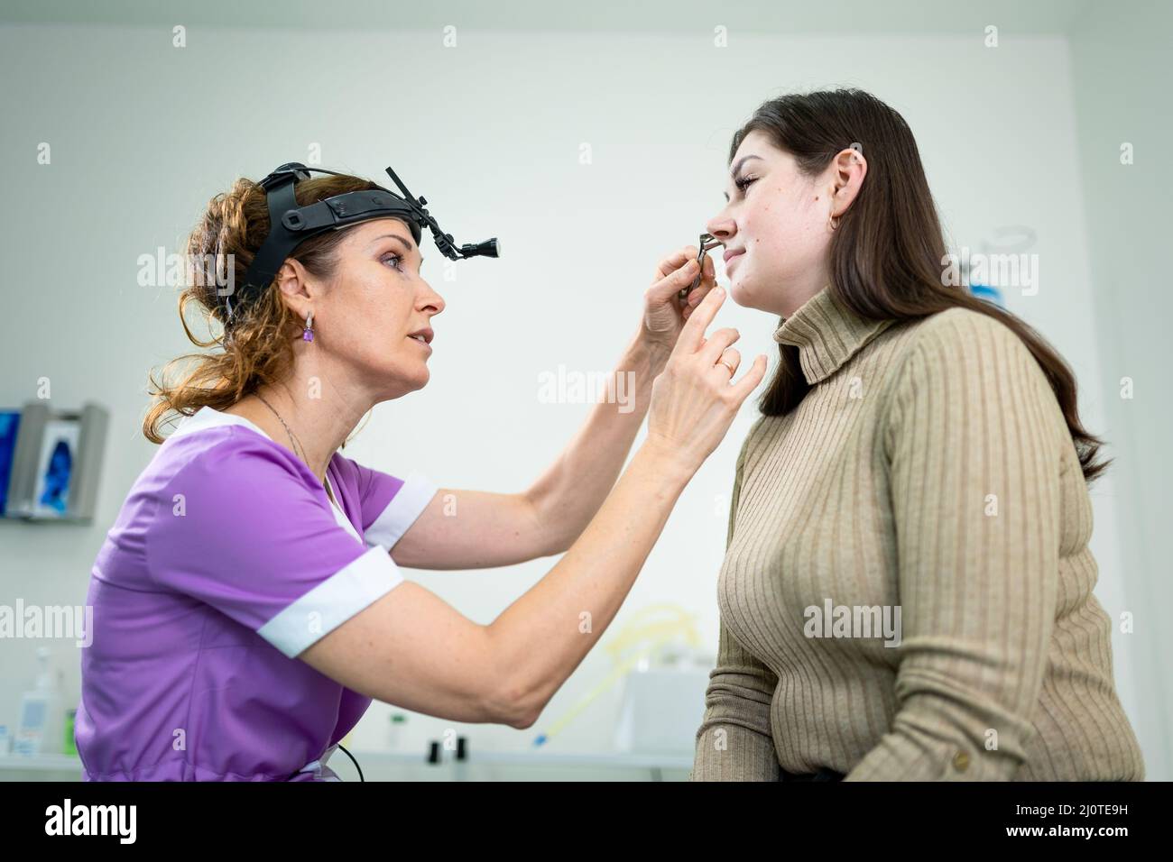 Professional female doctor otorhinolaryngologist doing nose examination with otoscope in modern hospital. Nasal congestion, sinu Stock Photo