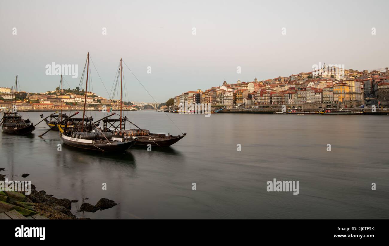Traditional boats loaded with wine barrels moored in the Douro river opposite the old town riverbank in the morning. Stock Photo