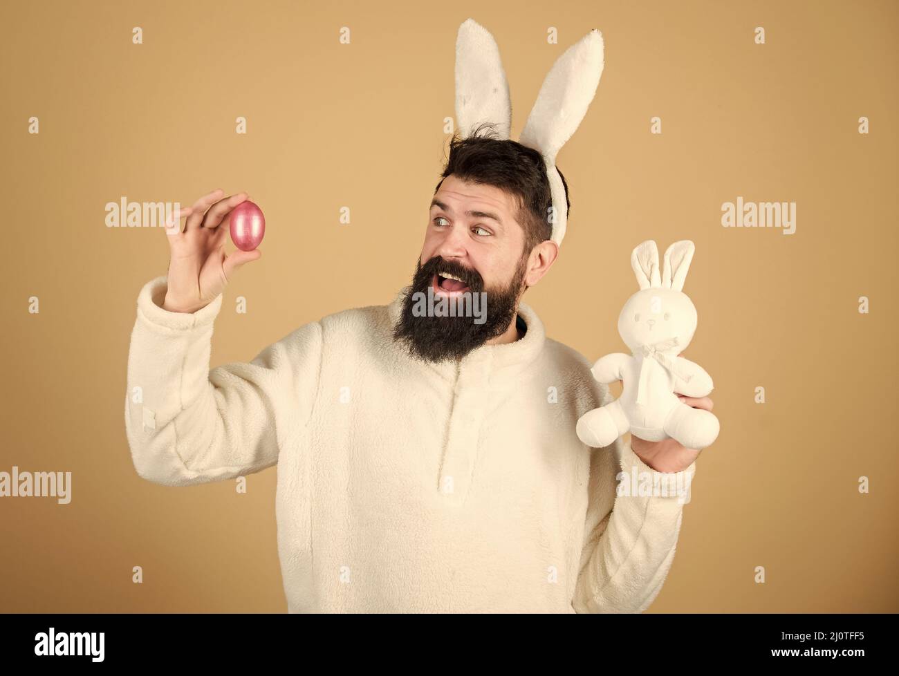 Easter activities concept. Weirdo concept. Celebrate Easter. Guy bearded hipster weird bunny with long white ears beige background. Easter rabbit. Man Stock Photo