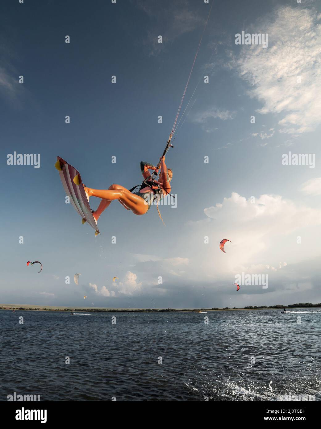 Professional athlete kitesurfer young caucasian woman doing a trick in the air against the backdrop of the sunset sky and clouds Stock Photo