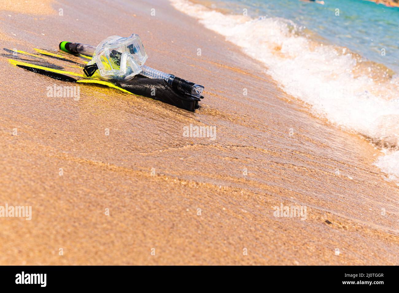 Snorkeling equipment on the sand with ocean waves splashing the water. Black fins, black mask, snorkel on sandy texture backgrou Stock Photo