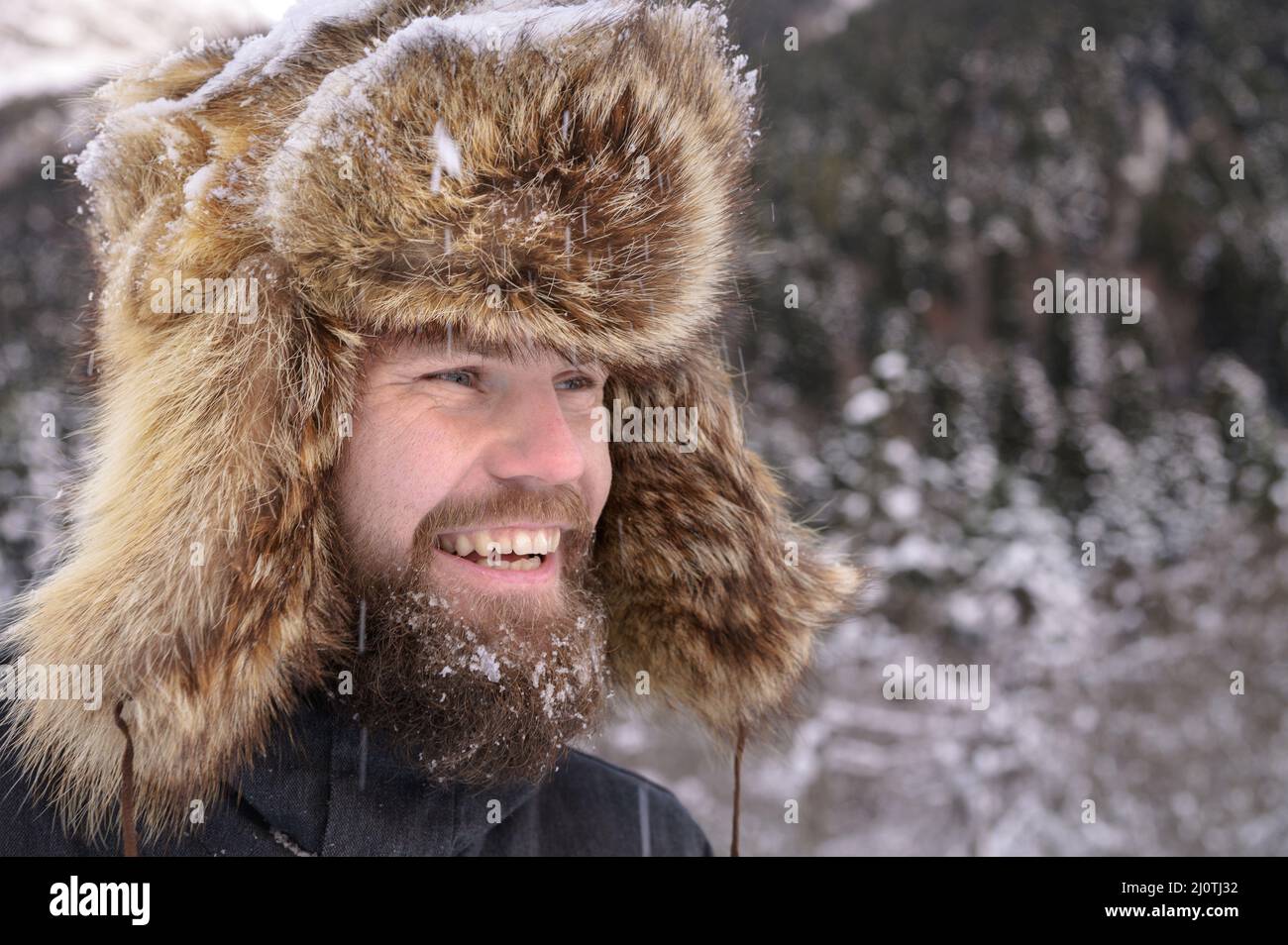 Man in a fur winter hat with ears smiling portrait on a background of a winter forest Stock Photo