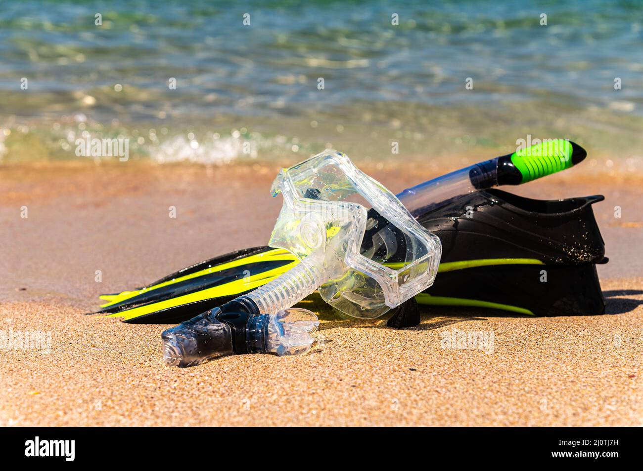 Snorkeling equipment on the sand with ocean waves splashing the water. Black fins, black mask, snorkel on sandy texture backgrou Stock Photo