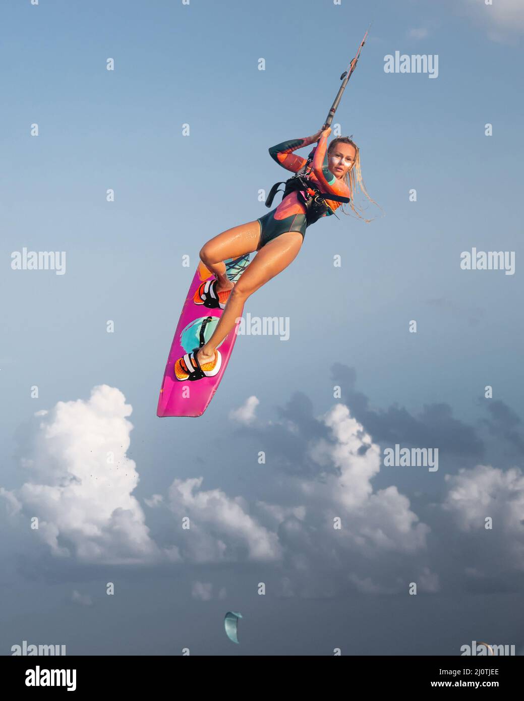 Professional athlete kitesurfer young caucasian woman doing a trick in the air against the backdrop of the sunset sky and clouds Stock Photo