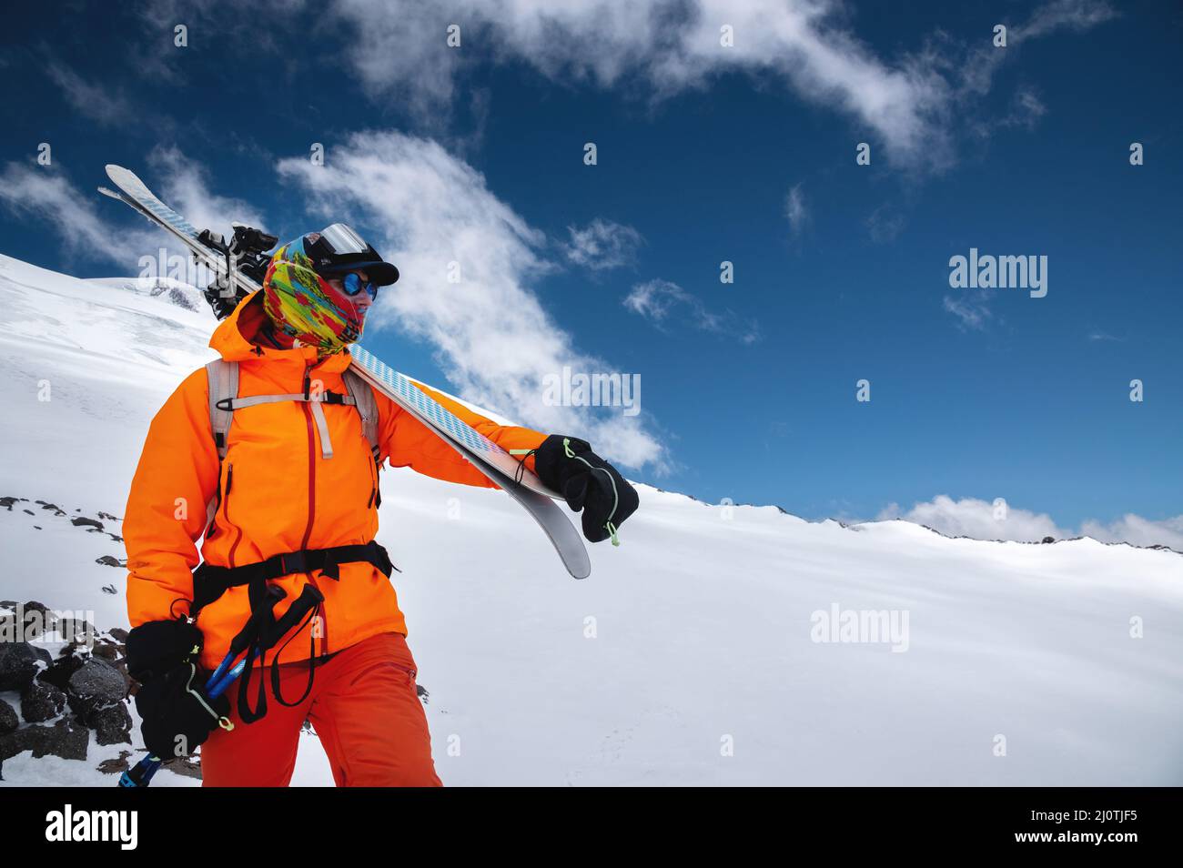 Mountain portrait of a professional freeride skier in orange clothing with  ski poles and skis on his shoulders. Stands high in t Stock Photo - Alamy