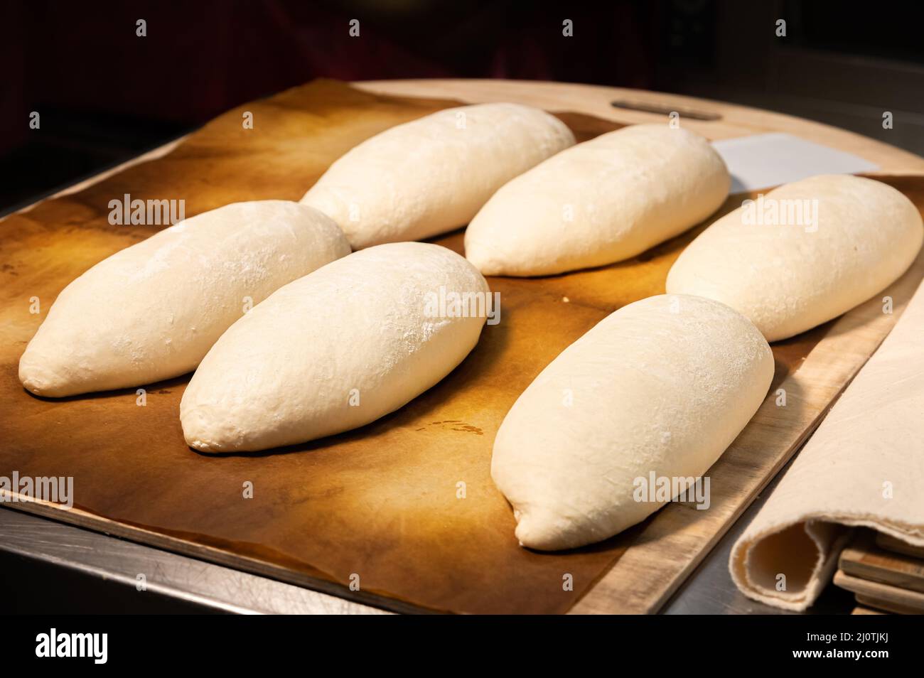 Raw loaves of french bread lying on a wooden tray on a table in a bakery Stock Photo