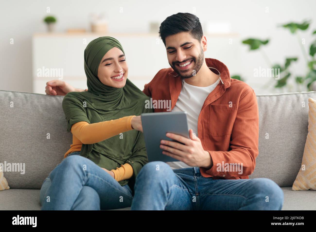 Happy Middle Eastern Spouses Using Digital Tablet Sitting At Home Stock Photo