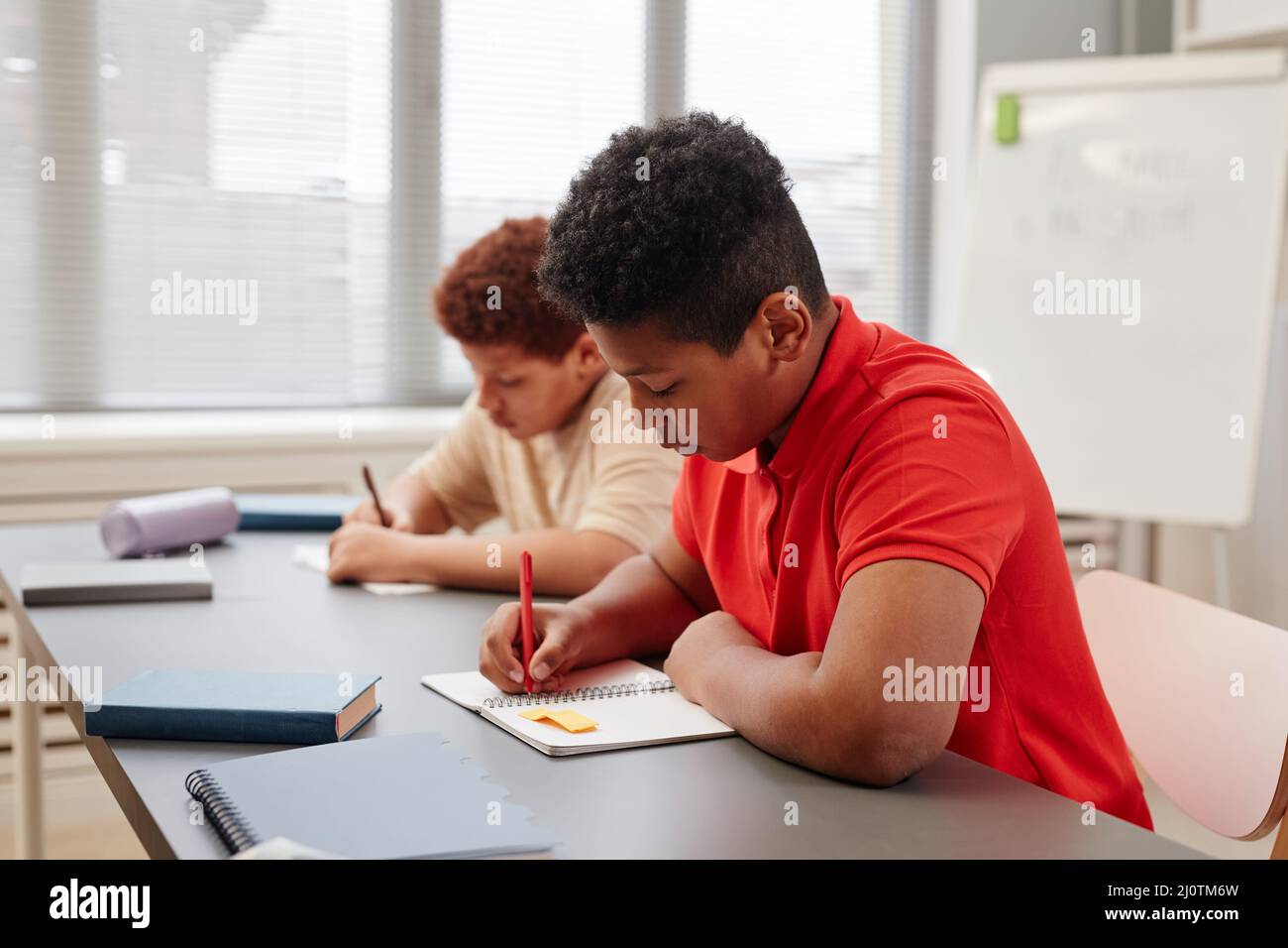 Side view portrait of African American teenage boy writing in notebook ...