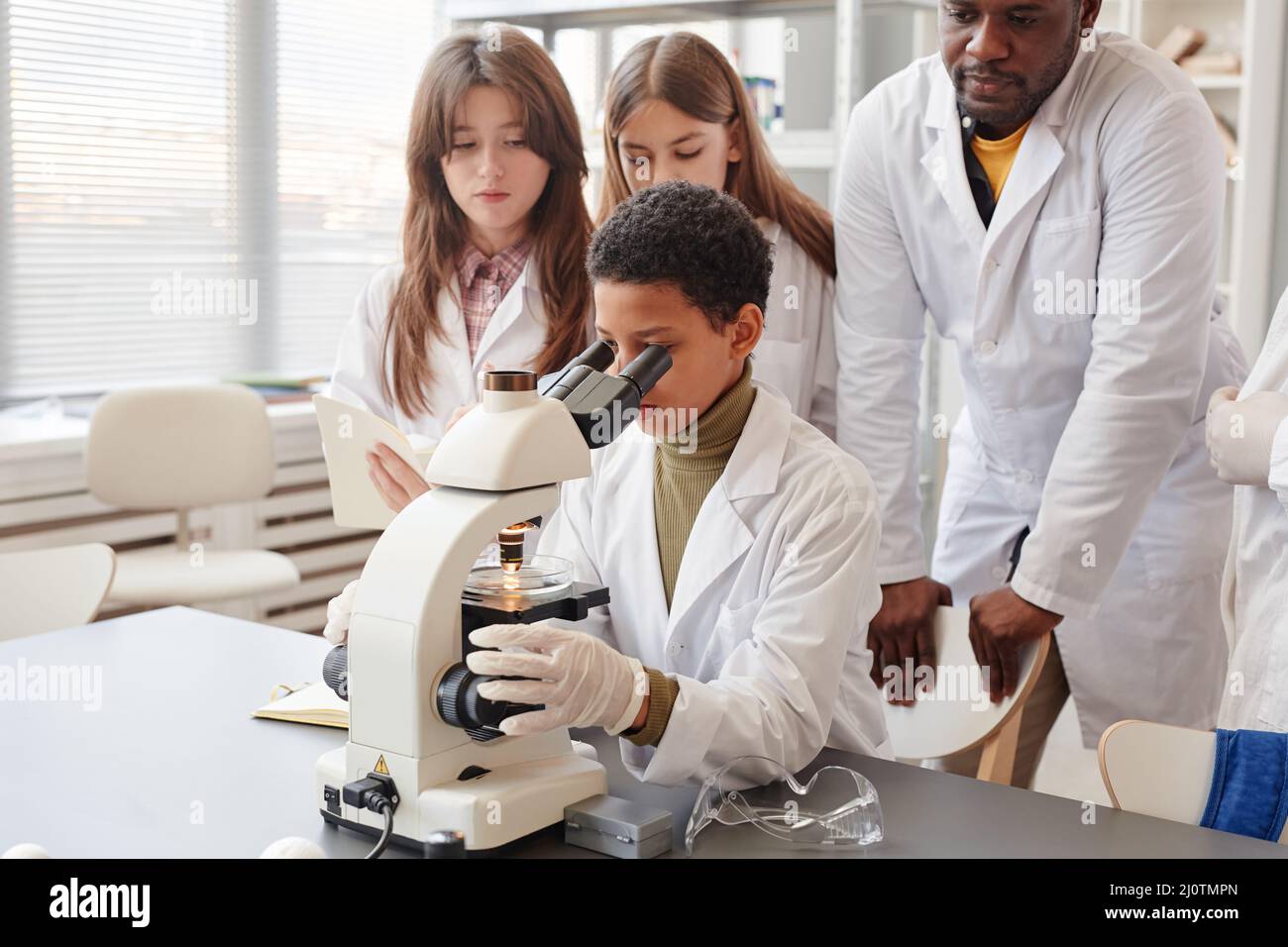 Portrait of young black girl looking into microscope with while doing ...