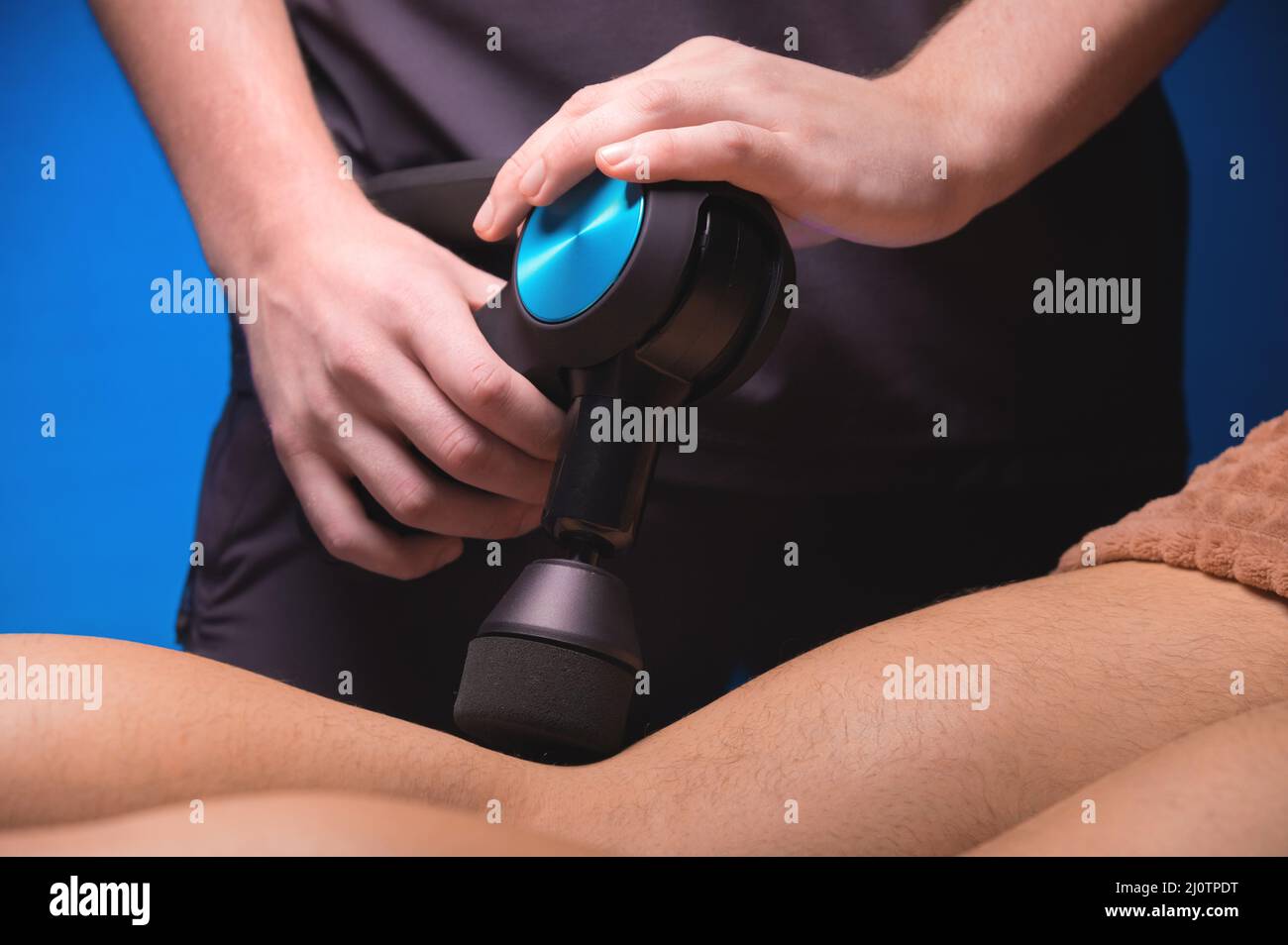 Close-up of a professional male masseur stimulates the leg muscles of a male patient in a dark spa room for massage. Percussion Stock Photo