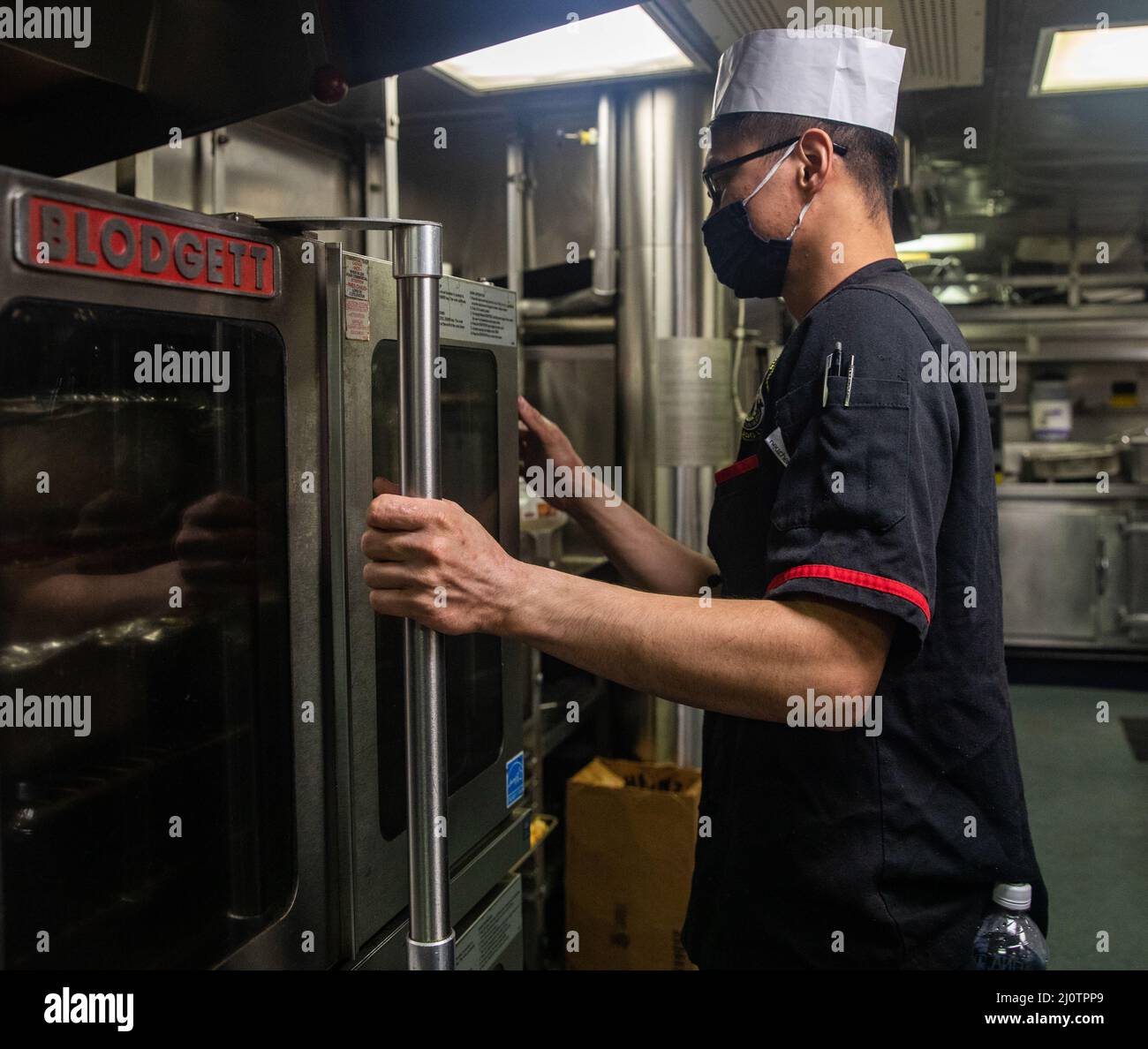EAST CHINA SEA (Jan. 26, 2022) Culinary Specialist 3rd Class Glenmark Gervacio, from Queens, N.Y., places a tray of food in an oven in the galley aboard Arleigh Burke-class guided-missile destroyer USS Ralph Johnson (DDG 114). Ralph Johnson is assigned to Task Force 71/Destroyer Squadron (DESRON) 15, the Navy’s largest forward-deployed DESRON and the U.S. 7th fleet’s principal surface force. (U.S. Navy photo by Mass Communication Specialist 2nd Class Samantha Oblander) Stock Photo