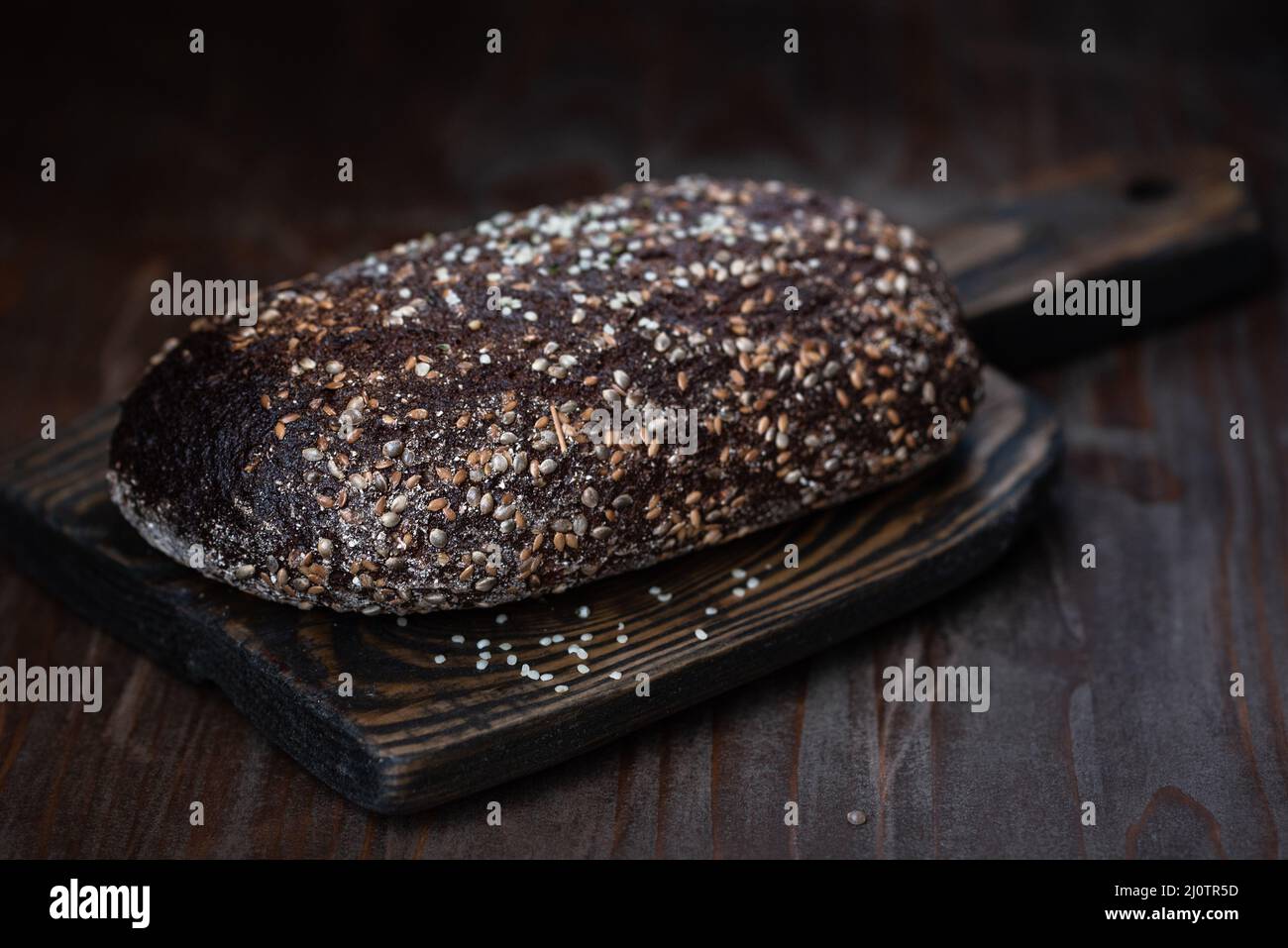 Whole rye bread covered with hemp seeds on the old wooden board Stock Photo