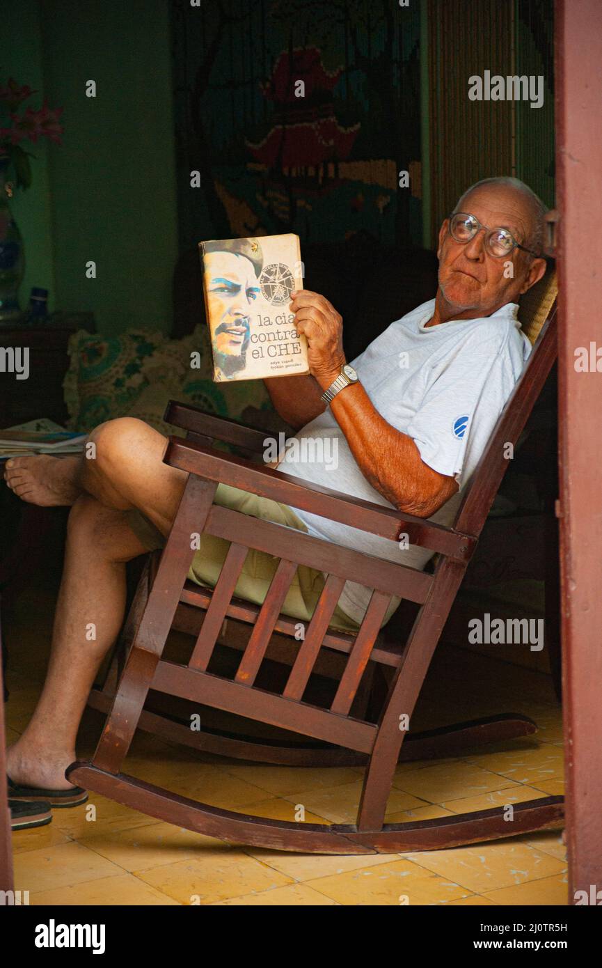 Cuban man in the doorway of his house reading a book about Cuban revolutionary hero Che Guevara in Camagüey, Cuba. Stock Photo