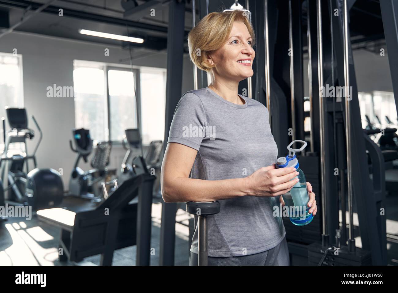 Sporty woman with bottle of water standing in gym Stock Photo - Alamy