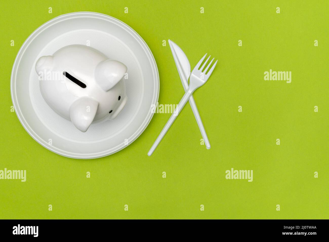 Piggy bank on the white disposable plate with a fork and knife Stock Photo