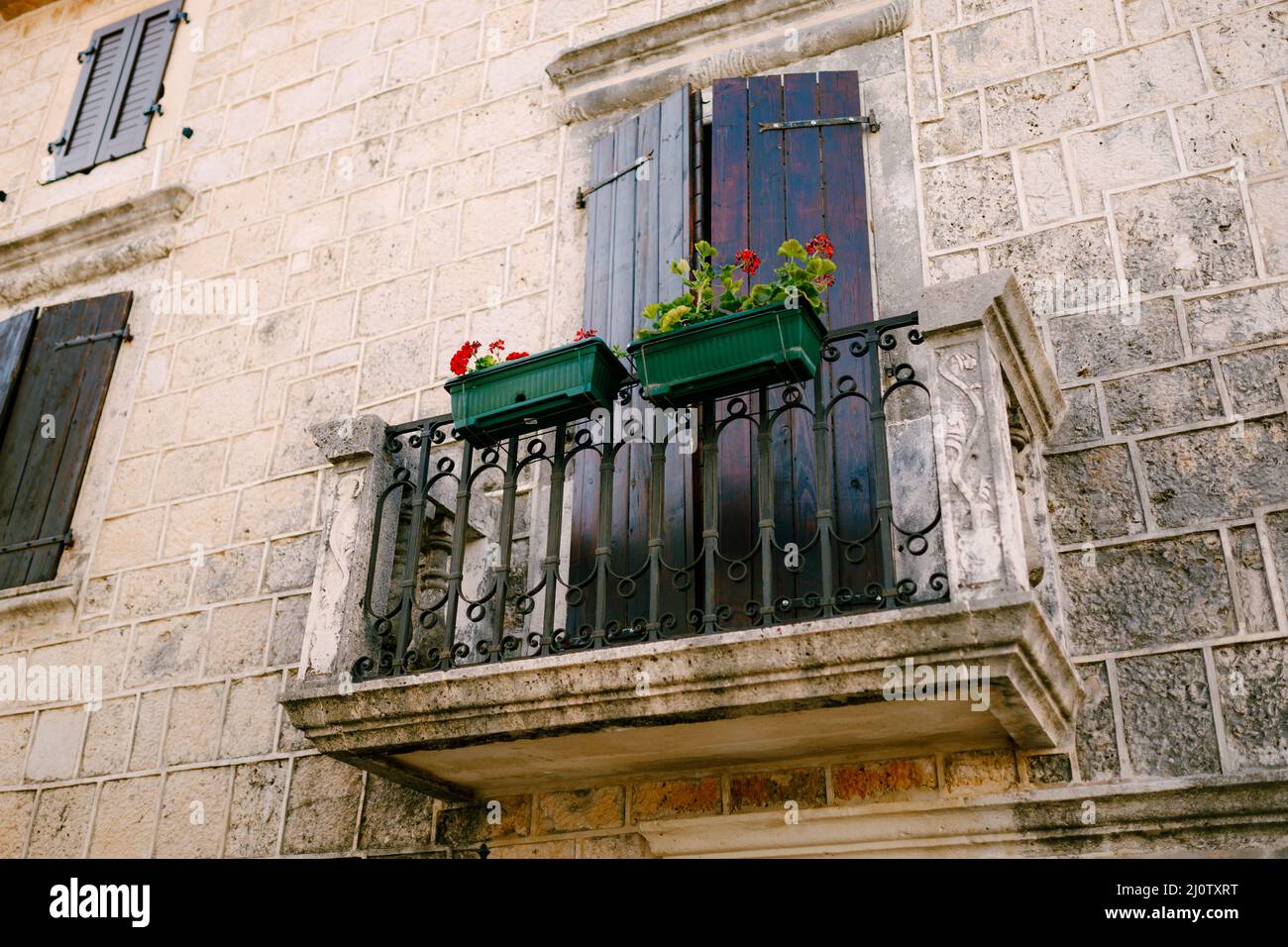 Stone balcony with a wrought iron lattice with flowerpots on the stone facade of the house Stock Photo