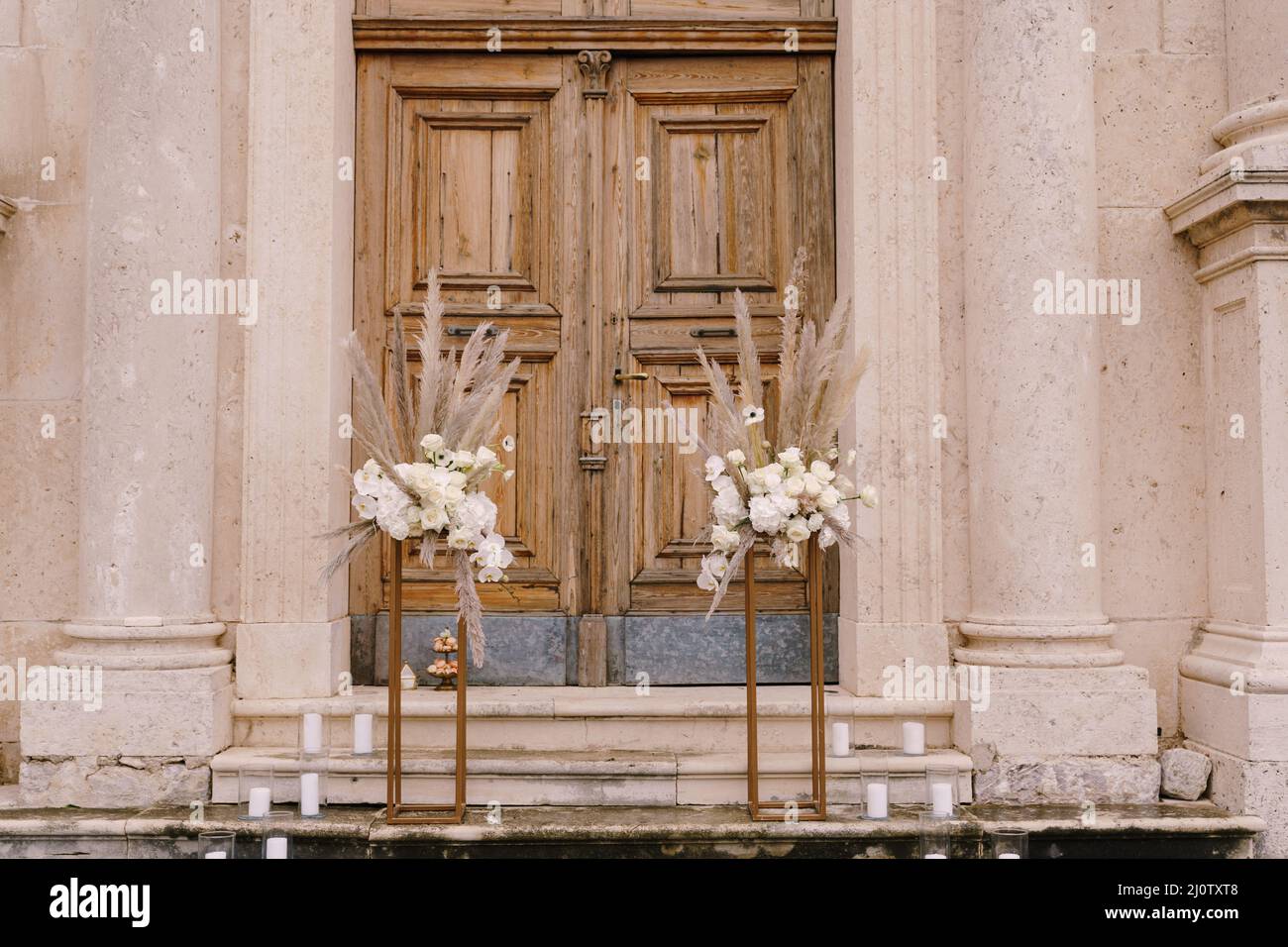 Bouquets of flowers stand on golden plinths in front of a wooden door of the church Stock Photo