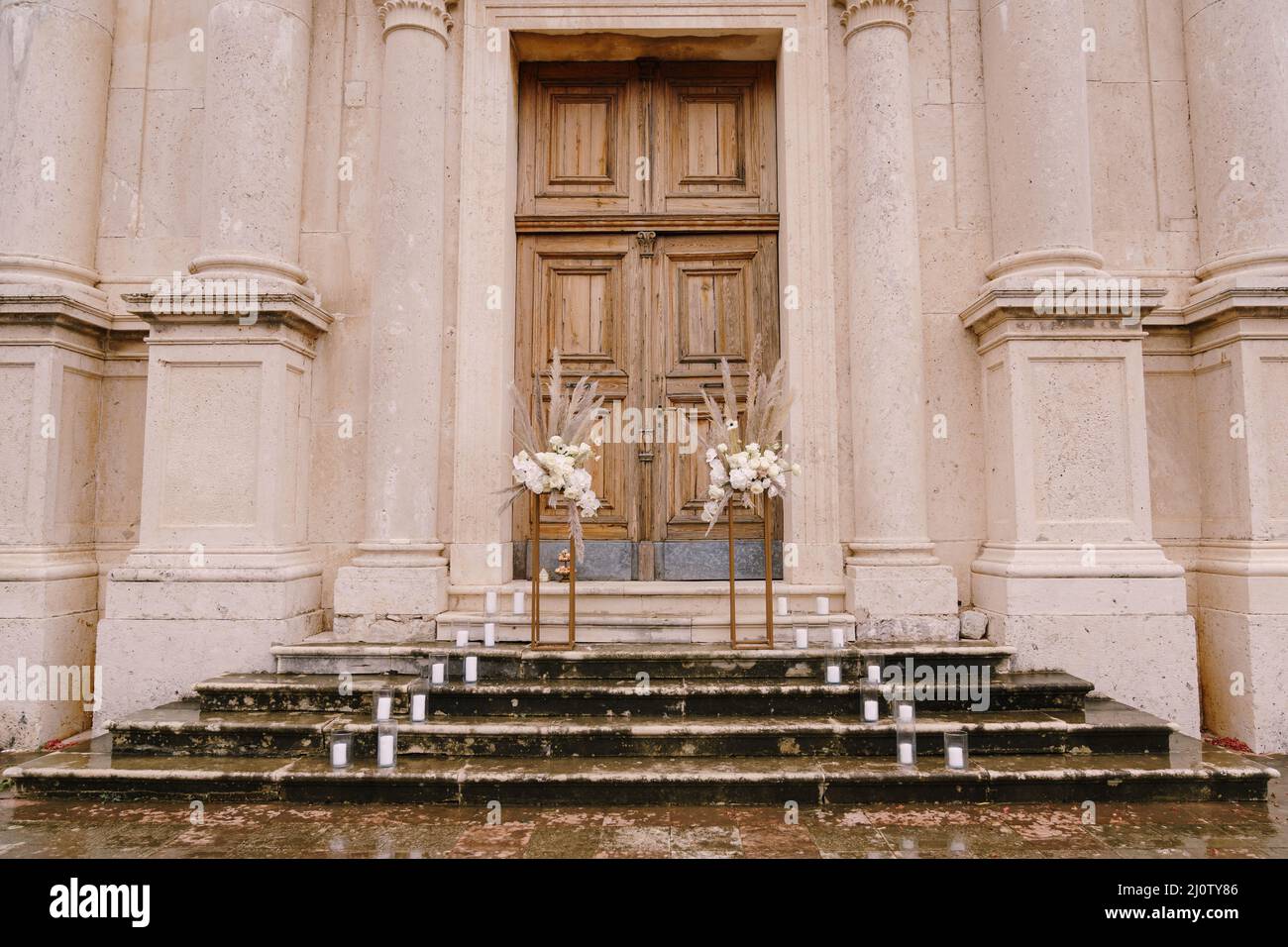Bouquets of flowers stand on golden plinths on the wet steps in front of a wooden door of the church Stock Photo