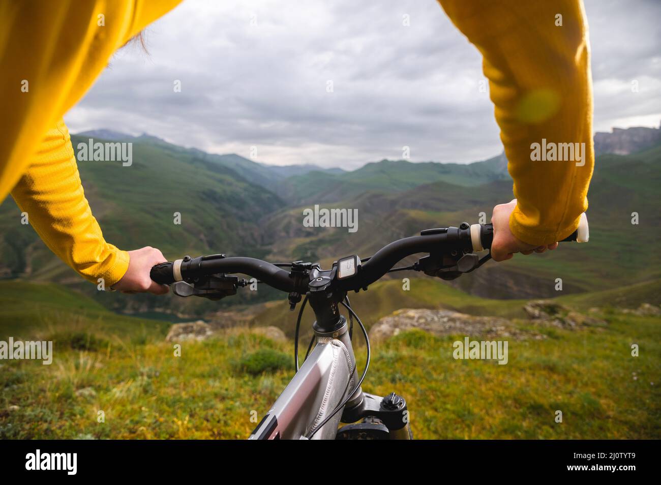 A close-up of the girl's hand cyclist on the handlebars of a mountain bike against the backdrop of epic rocks and mountains. Mou Stock Photo