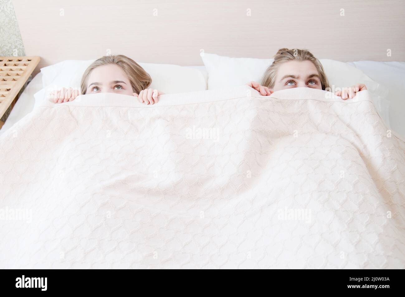A young couple in bed covers half of their faces with a blanket hiding and hiding behind a blanket. The concept of family-free p Stock Photo